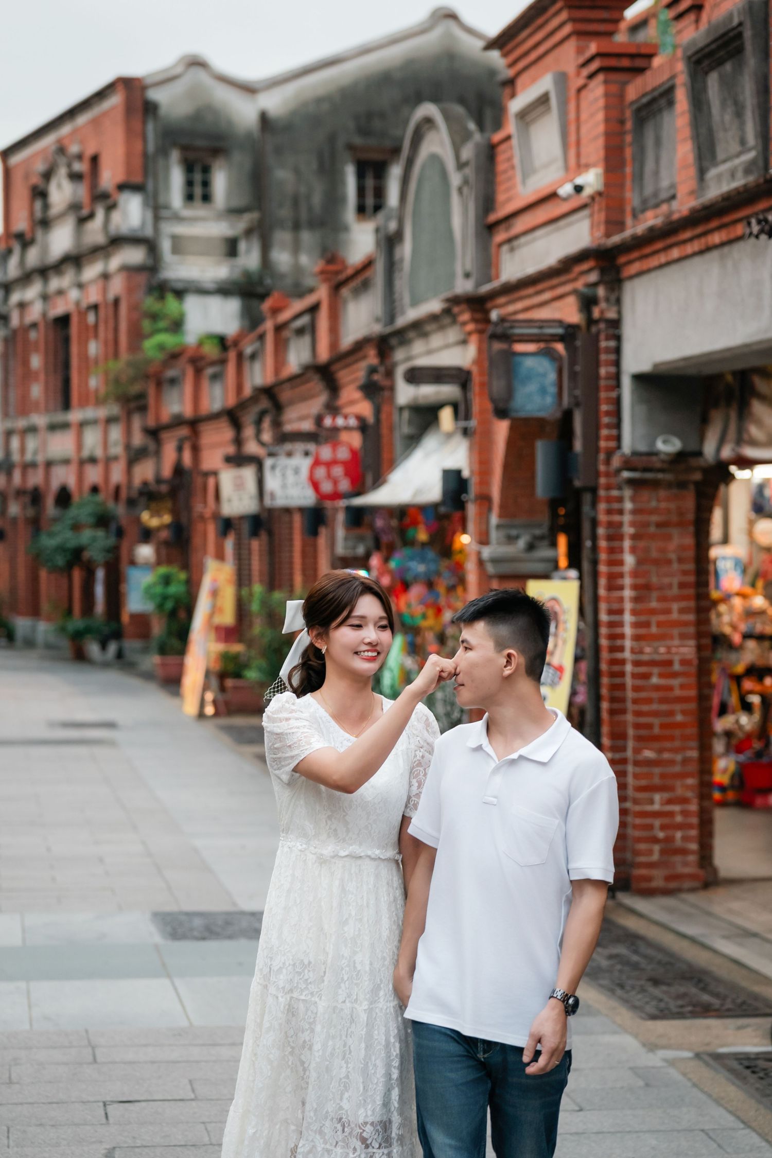 A couple shares a tender moment while strolling along a historic street with traditional red brick architecture.