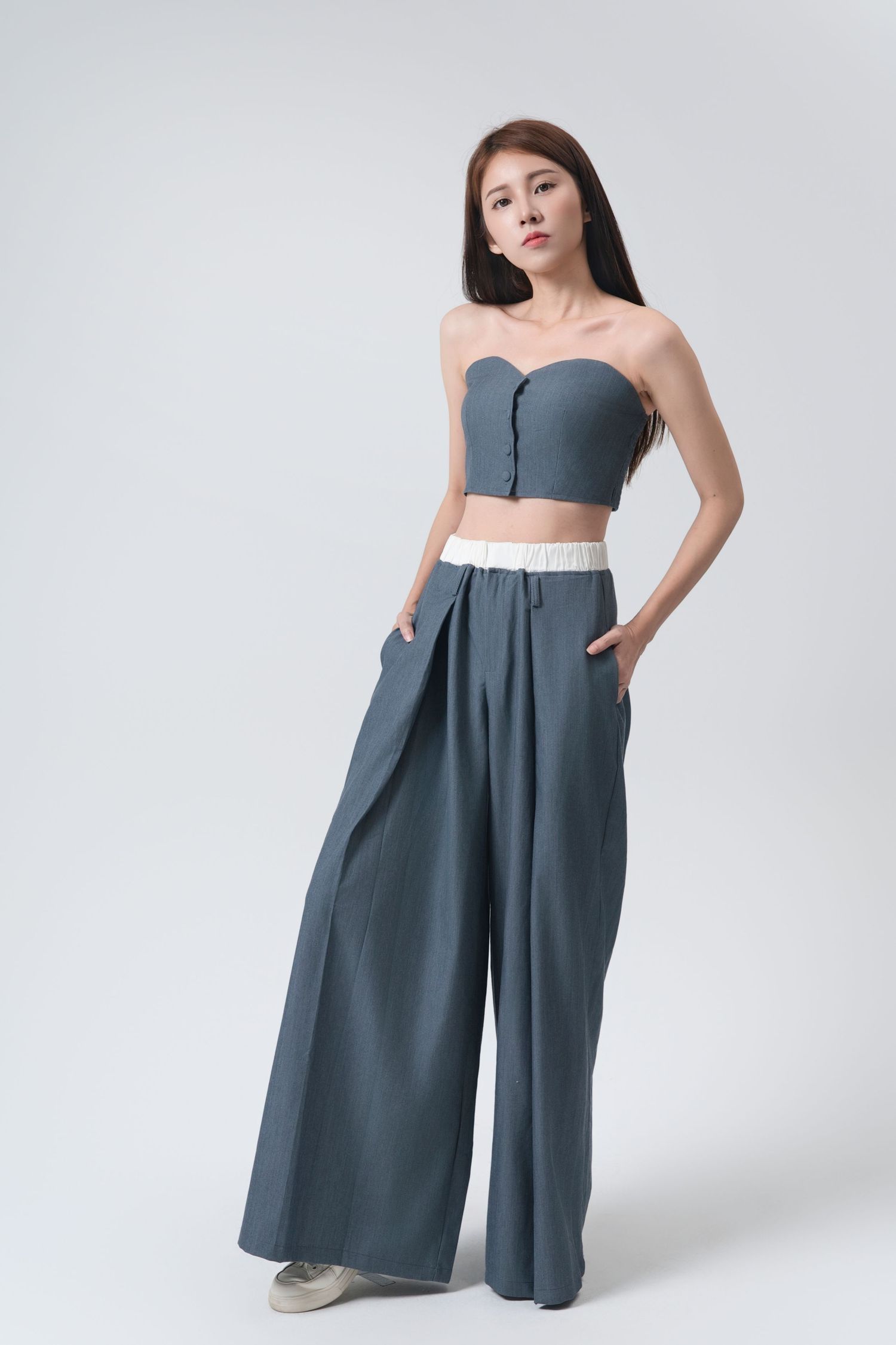 Woman wearing a modern gray wide-leg jumpsuit with pockets poses against white background in fashion photoshoot series.