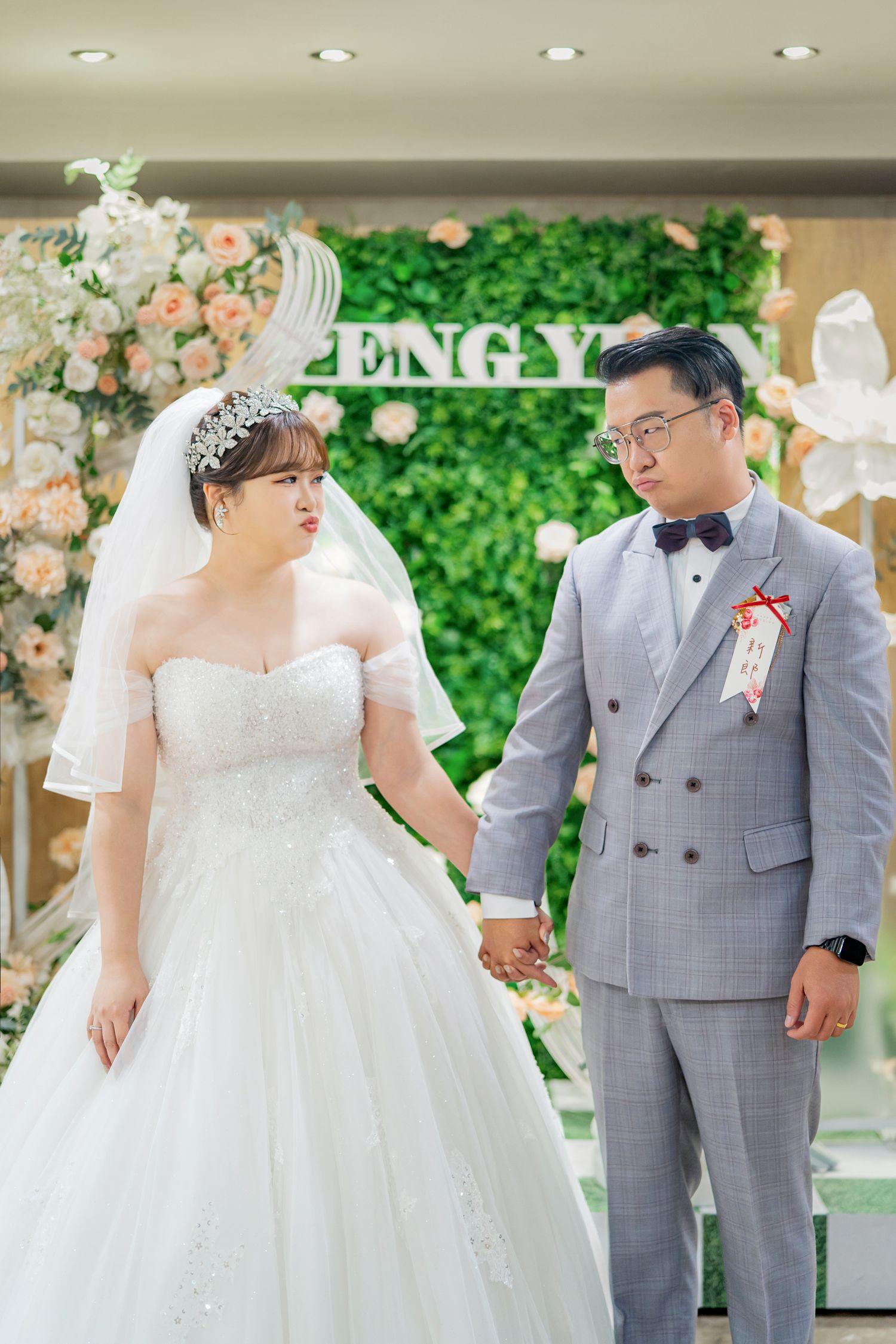 A romantic wedding scene with a couple in a white dress and grey suit holding hands in an elegant indoor venue.