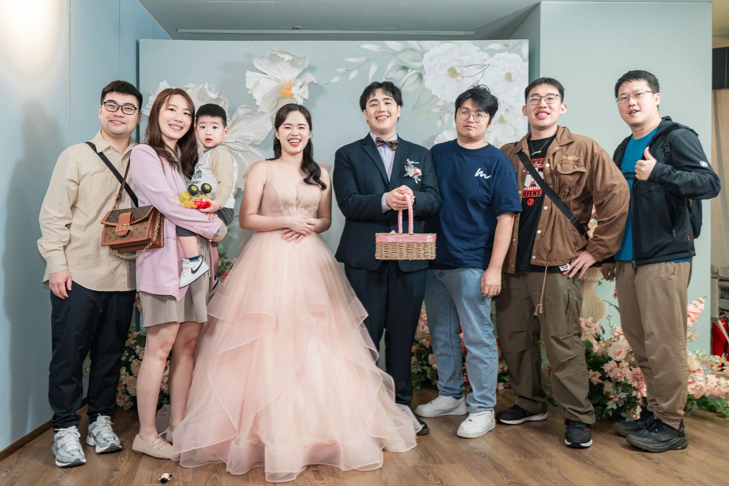 A group poses together at a formal event wearing a mix of pink dresses and casual attire.