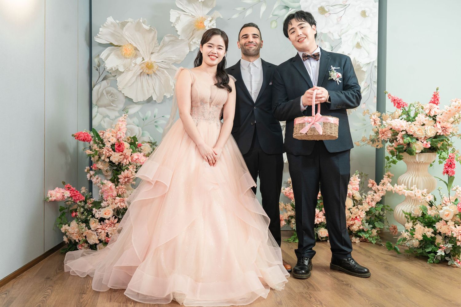 Wedding party poses playfully in front of floral backdrop with pink and white decorations.