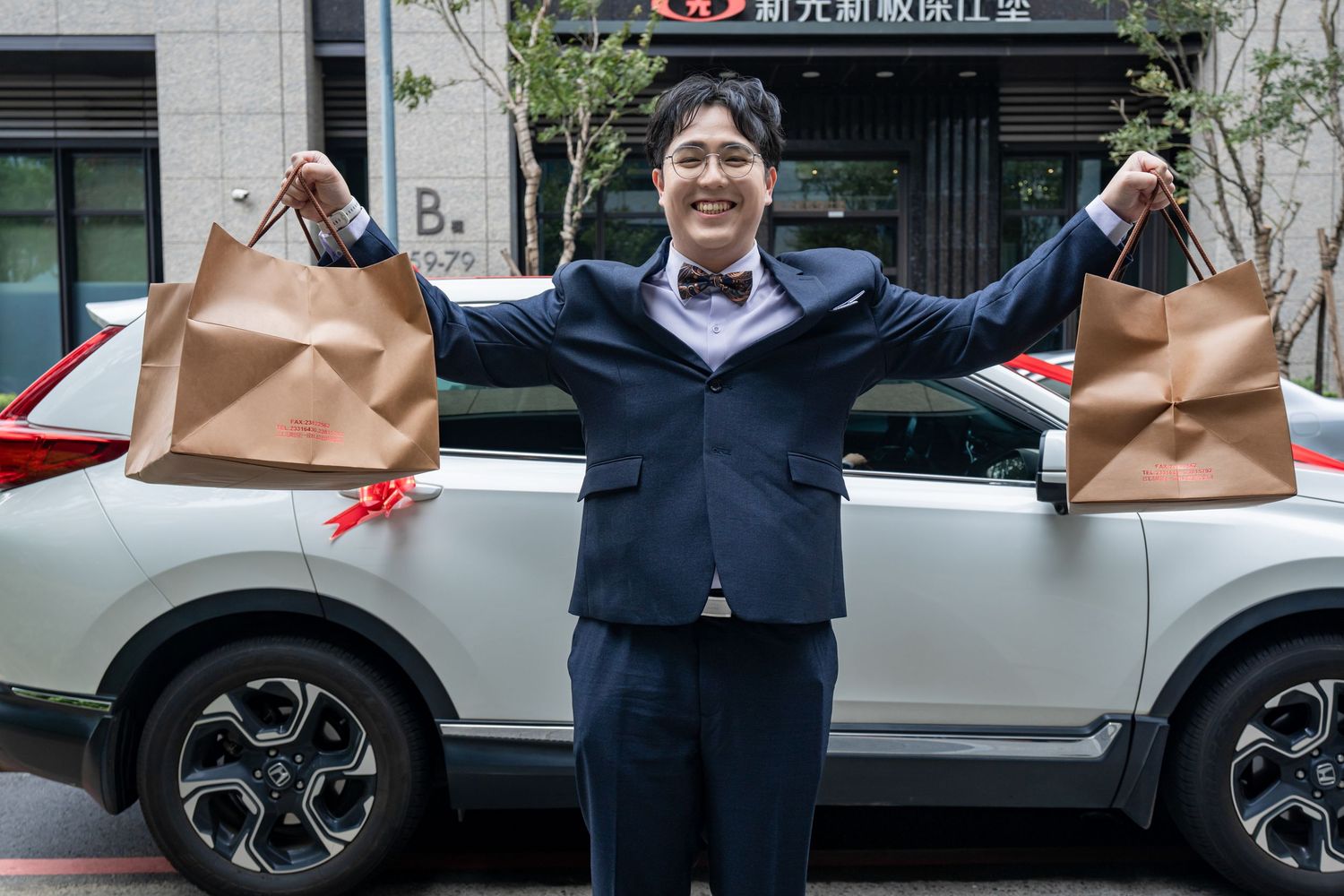Business professional stands with arms raised celebrating success outside an office building in an urban setting.