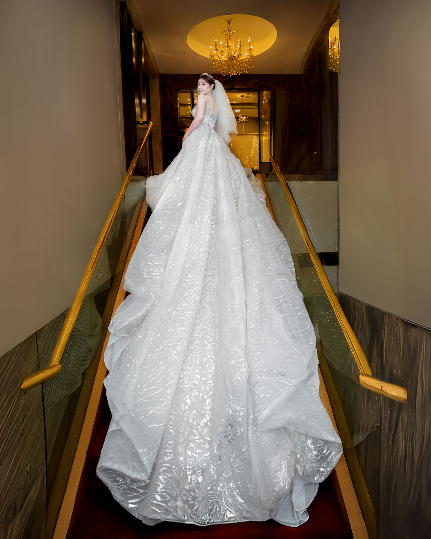 A stunning white lace wedding gown with a dramatic long train displayed in an elegant hotel hallway.