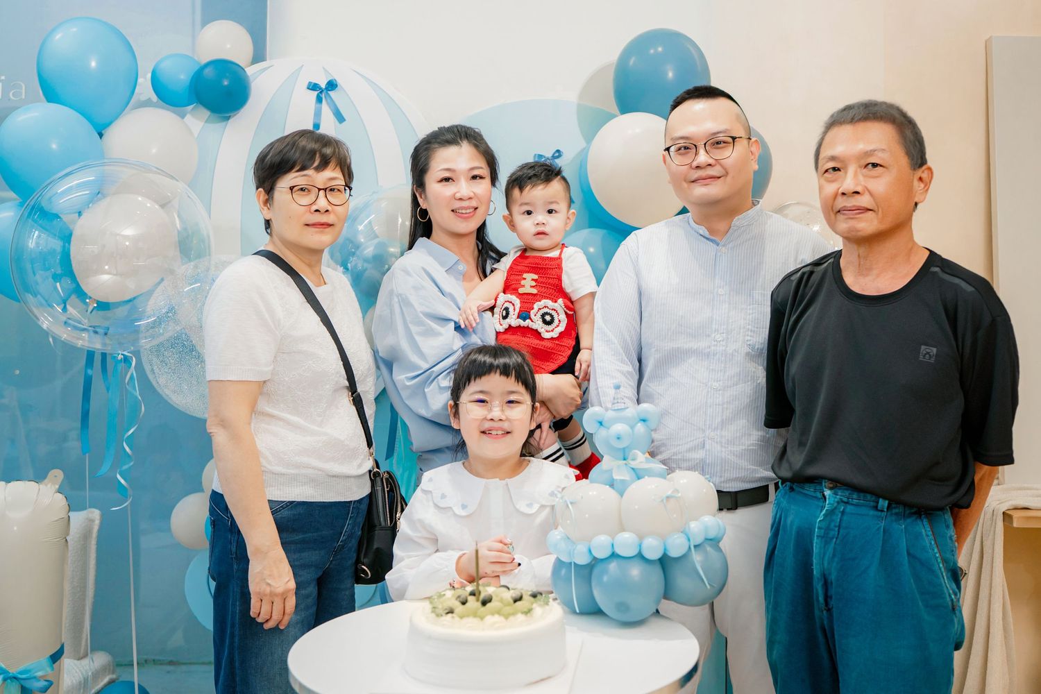 A group gathers at a celebration decorated with light blue balloons and festive party decoror.
