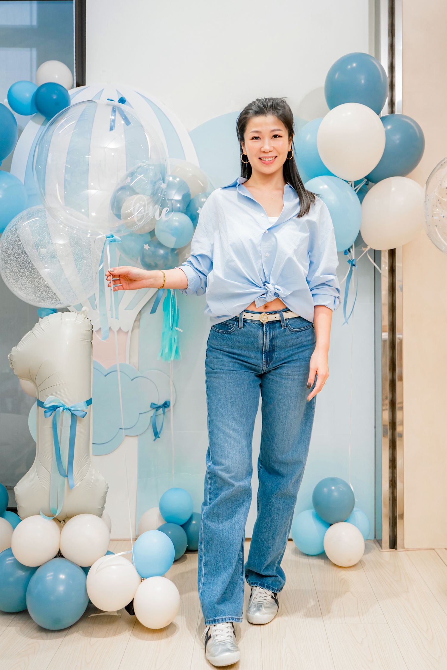 Festive party setup with blue and white balloons arranged against a light colored wall with someone in jeans.