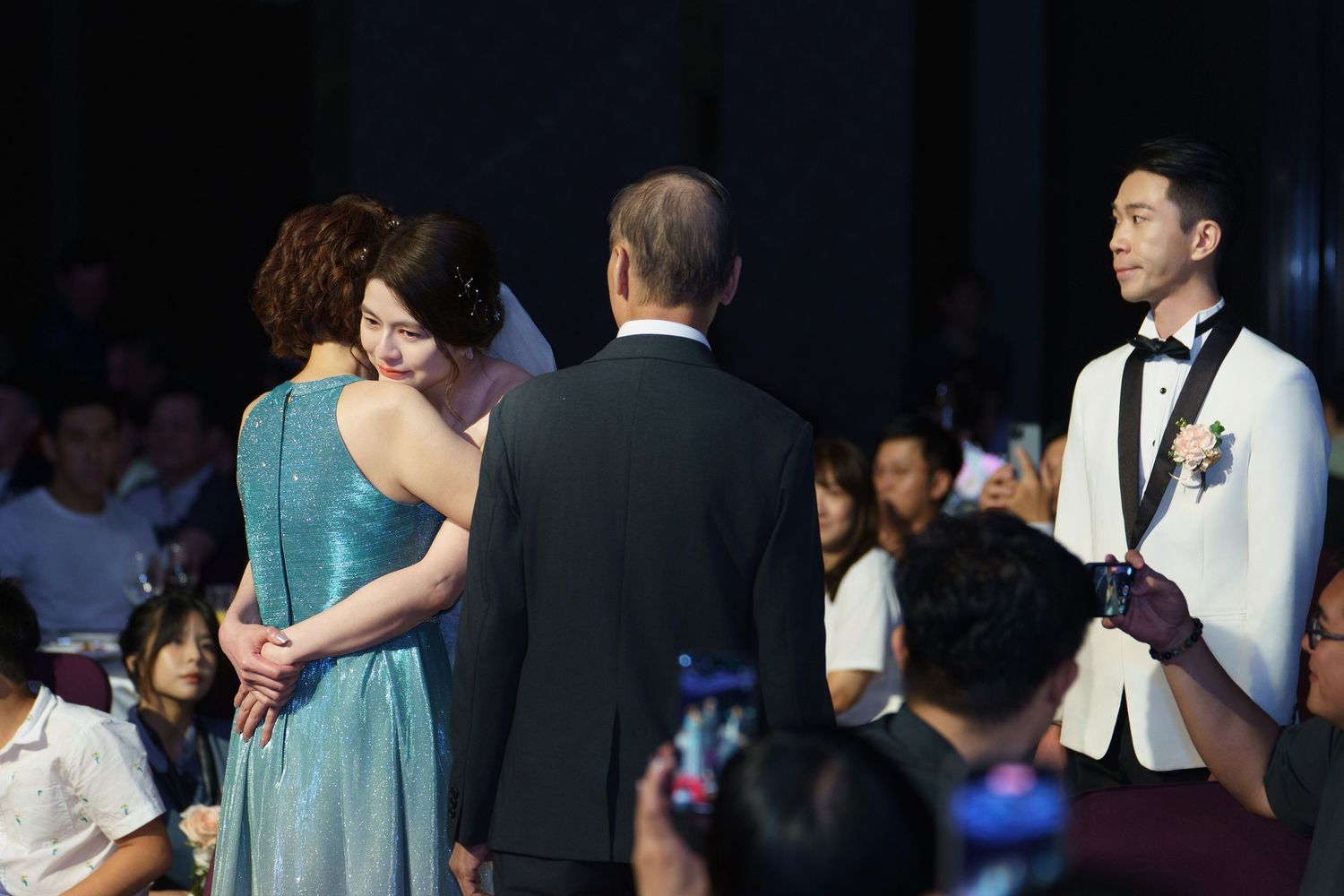 People dancing close together at a formal event wearing elegant evening attire and suits.
