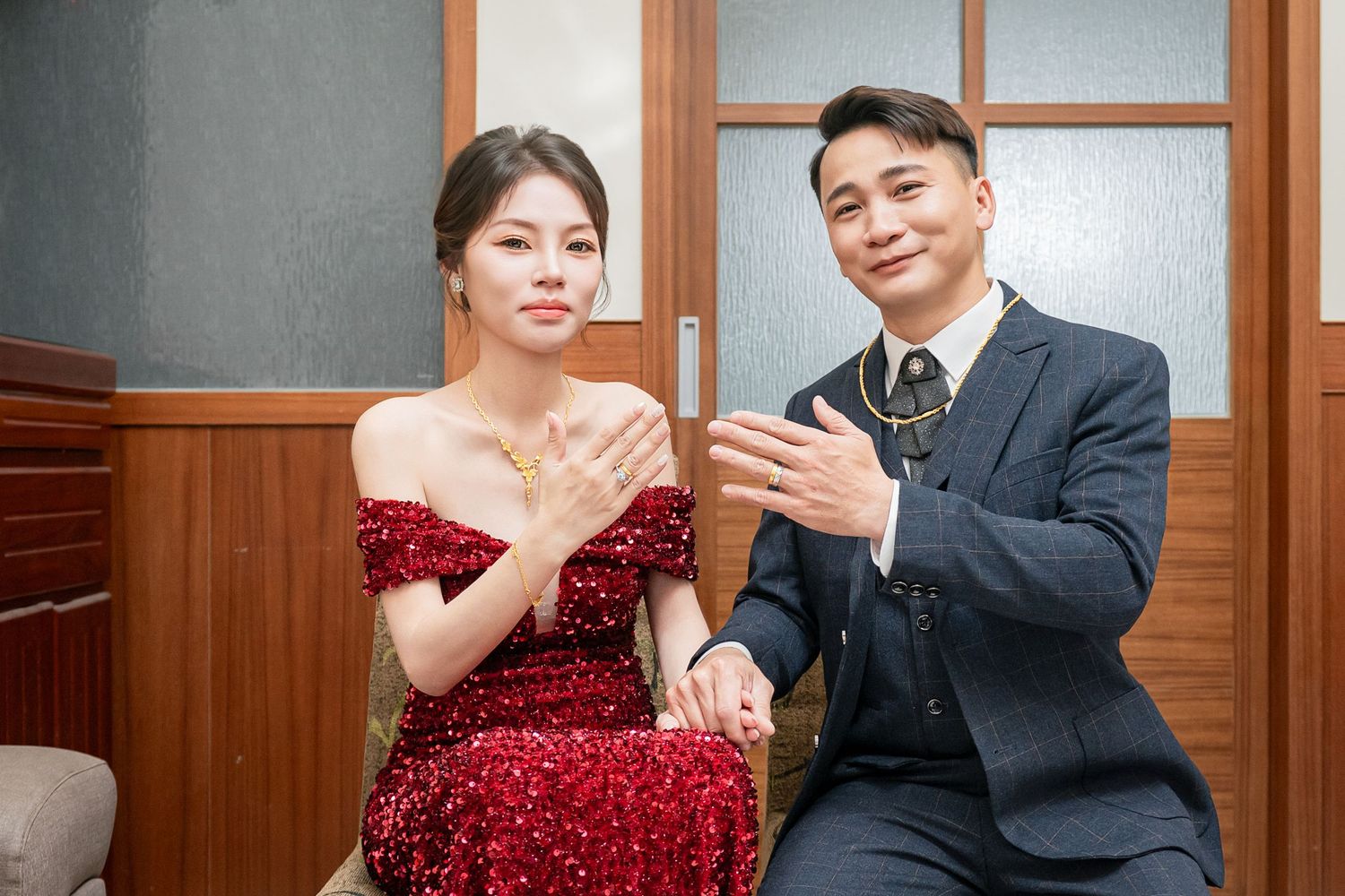 A couple poses together in formal attire, with the woman wearing a sparkling red gown and the man in a dark suit.