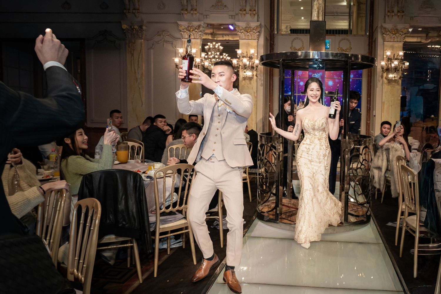 Wedding guests dance together during a reception celebration on a dance floor illuminated by warm lighting.