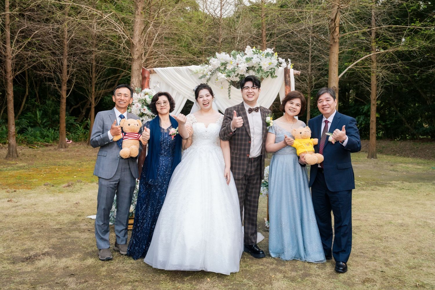 Wedding party in light blue bridesmaid dresses and dark suits poses together on grassy outdoor path.