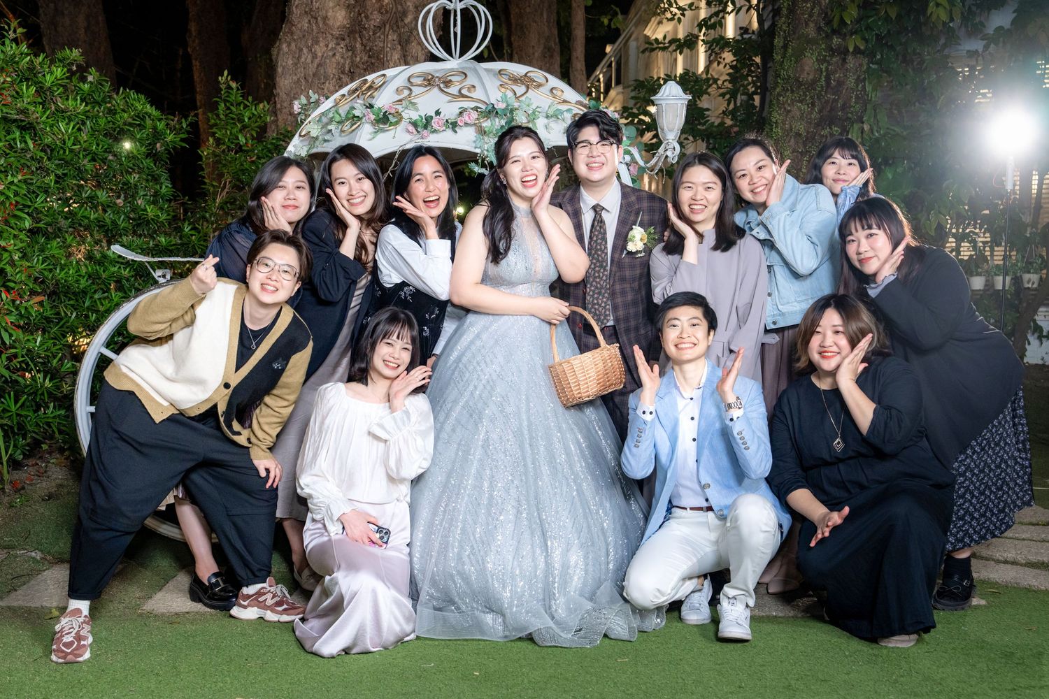 A group of friends in formal attire pose together at an outdoor evening celebration.
