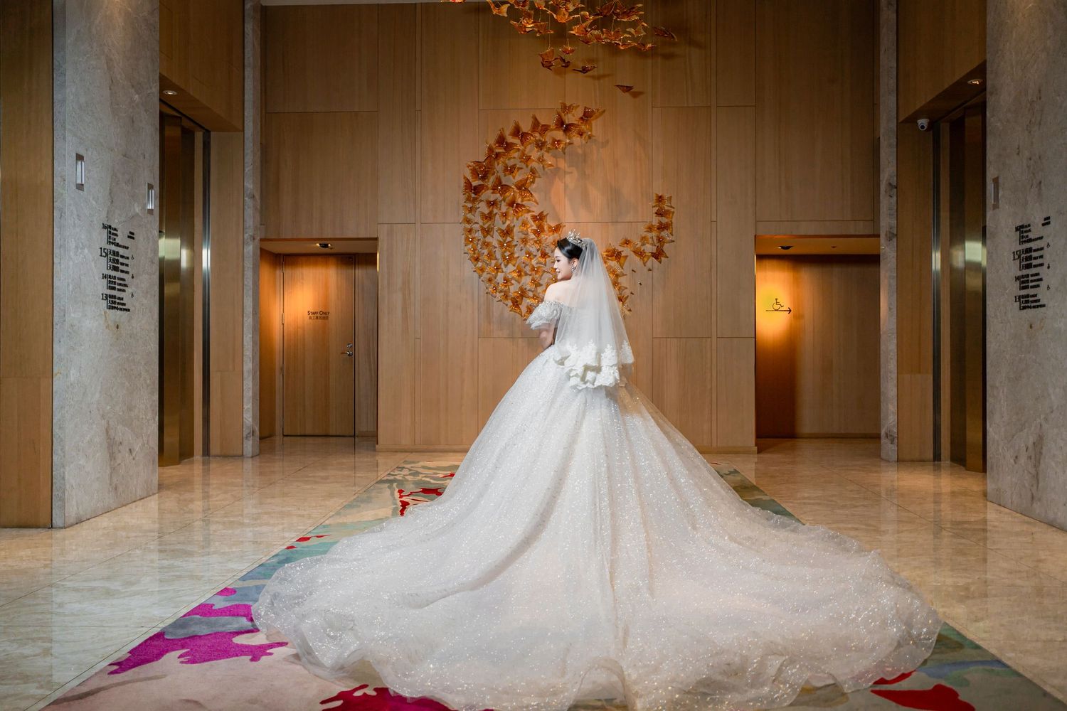 Bride in luxurious white wedding gown and long veil poses in elegant marble hallway with autumn leaf decor.