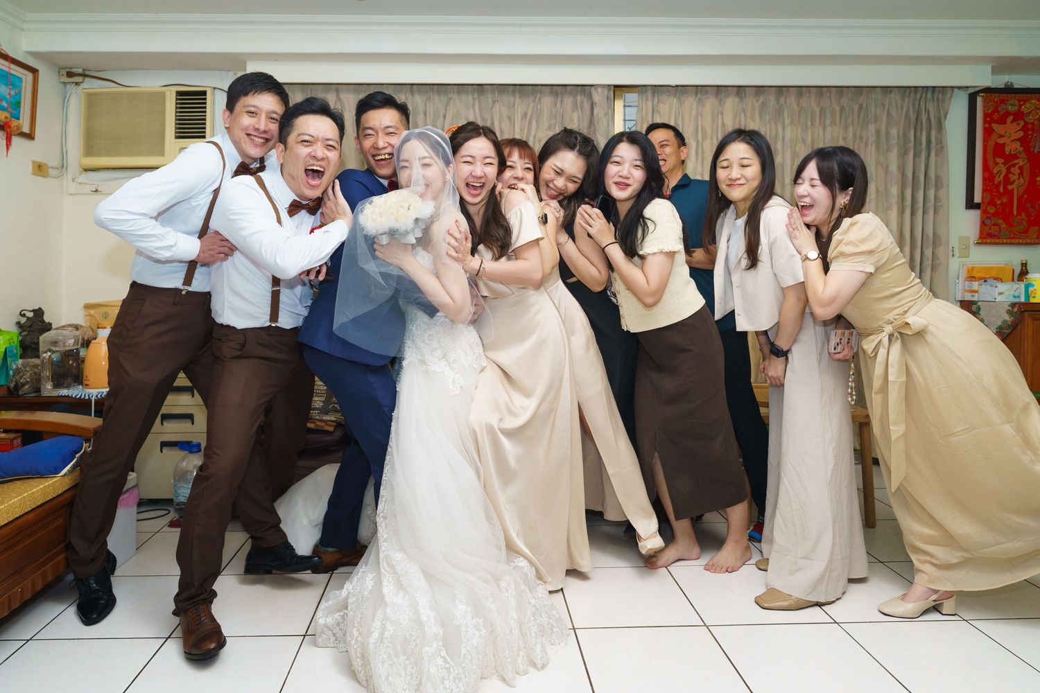 A festive wedding celebration with guests posing playfully together in formal attire at an indoor venue.