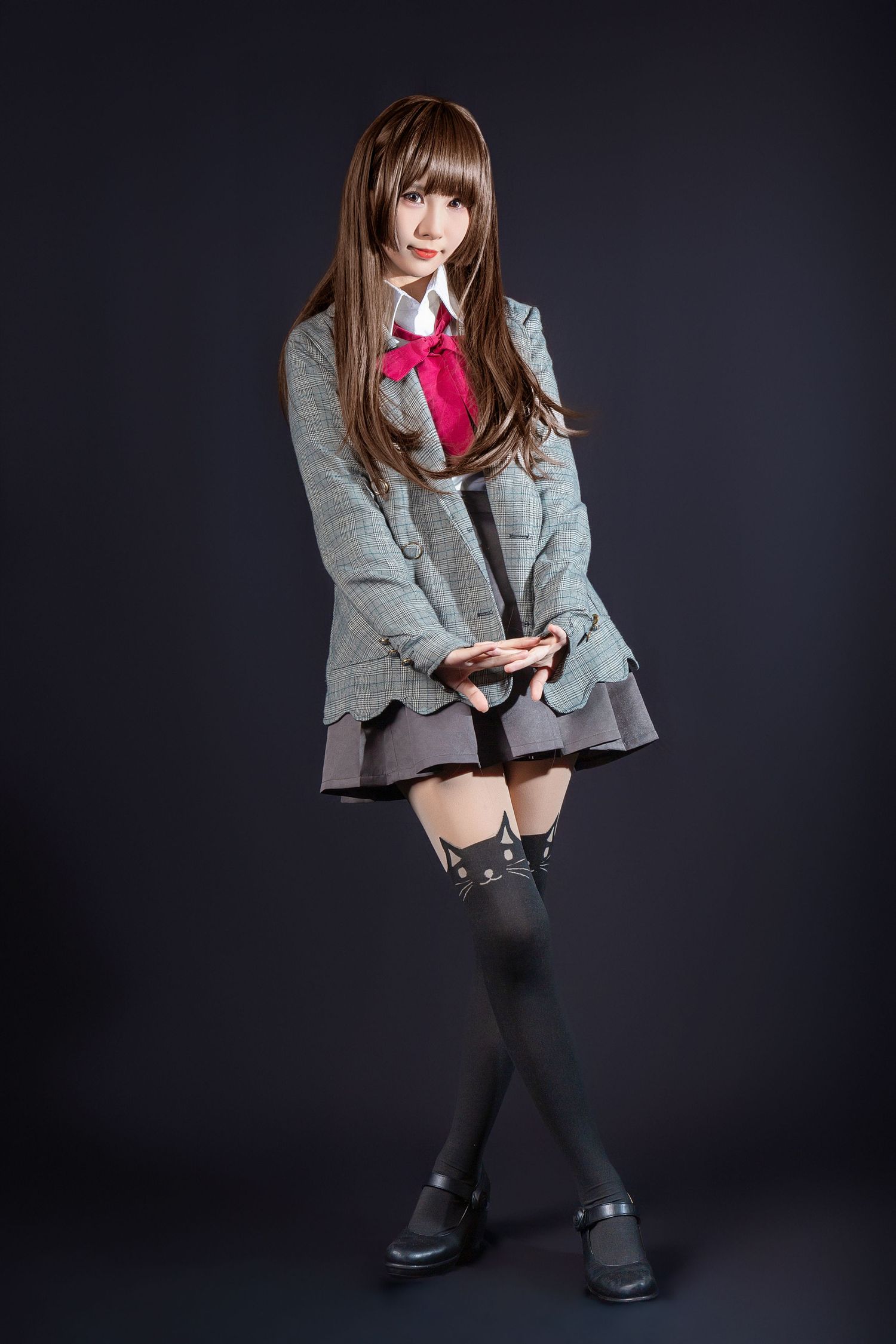 School uniform cosplay with gray blazer, red bow tie, pleated skirt, and knee-high socks against dark background.