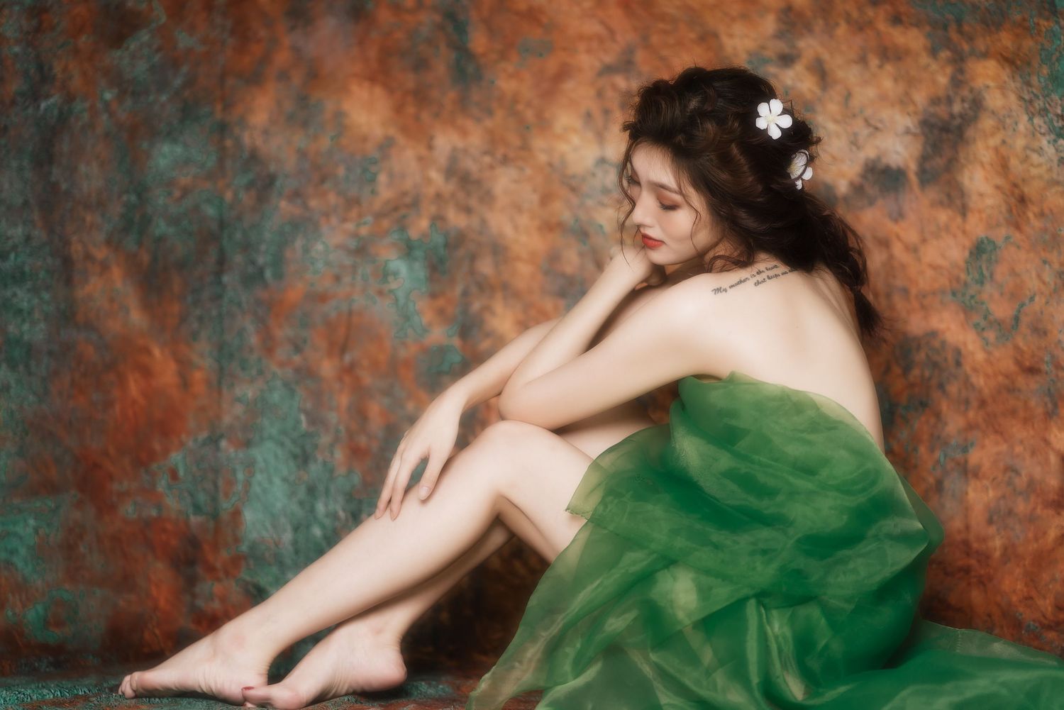 Artistic portrait of a figure in an emerald green dress resting against a textured rust and turquoise backdrop.