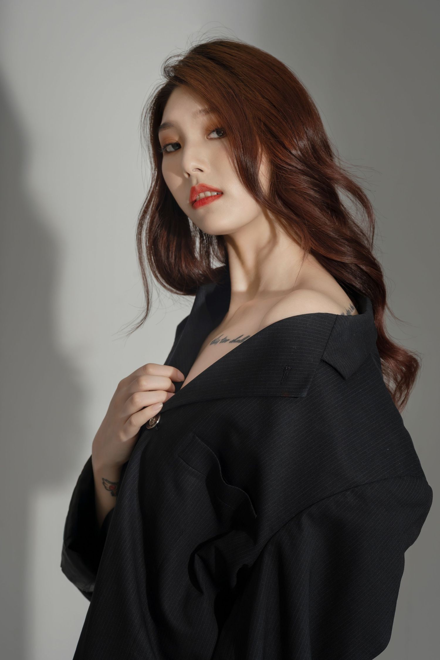 A person wearing a black oversized blazer poses against a light background with dramatic shadows.