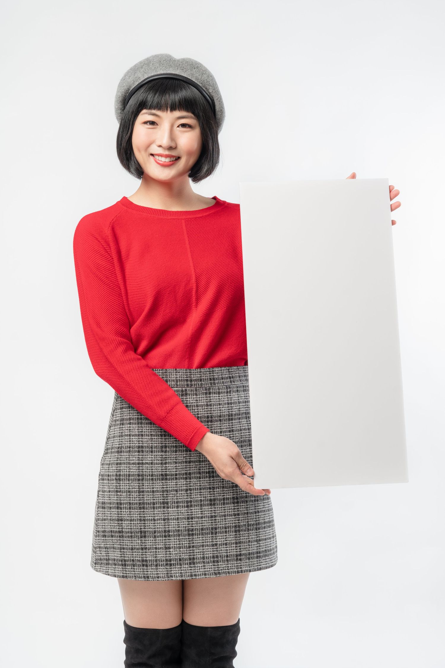Person wearing red sweater and plaid skirt holding blank white sign board against white background.