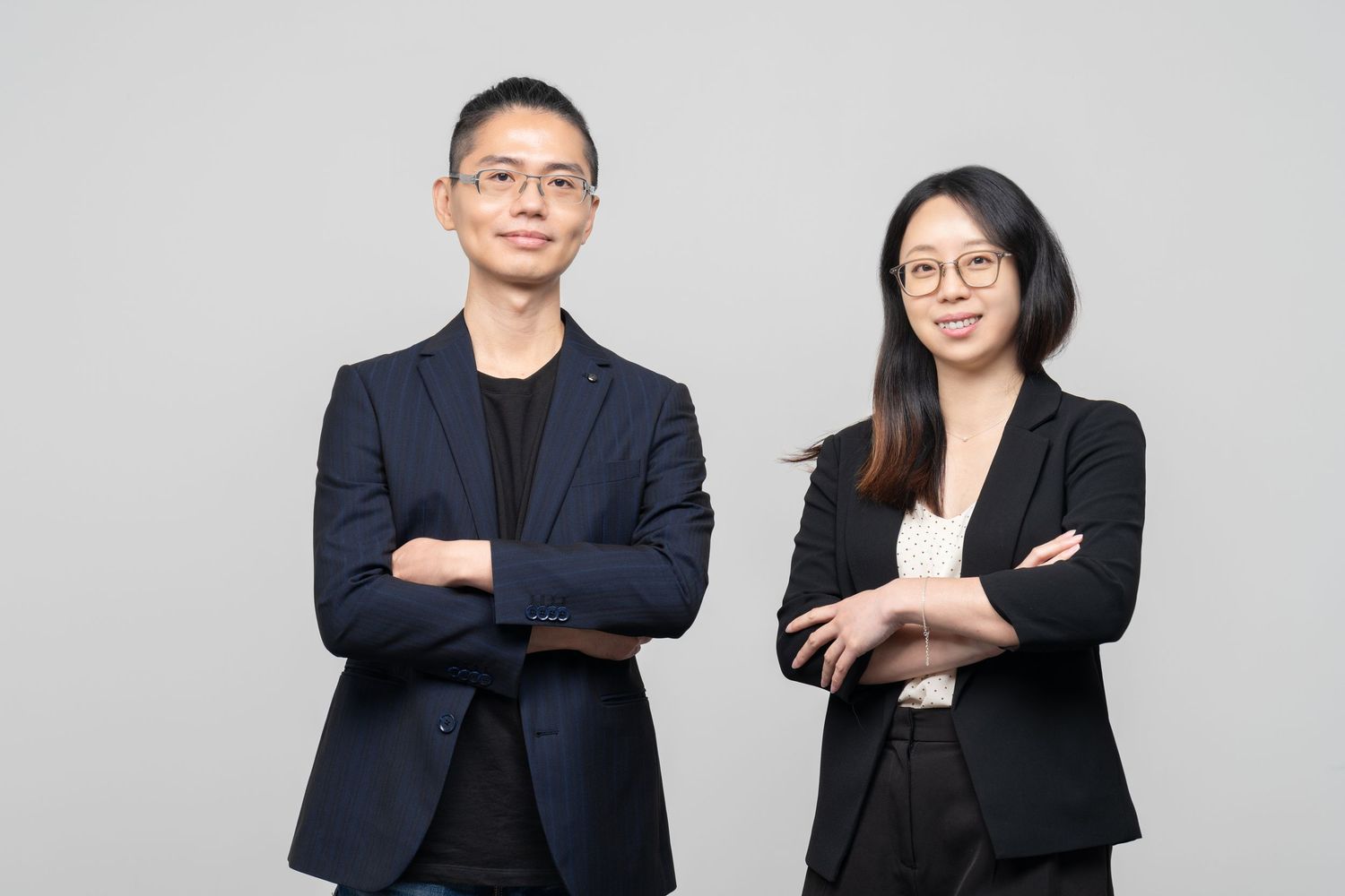 Two professionals in dark business attire stand with crossed arms against a light background.