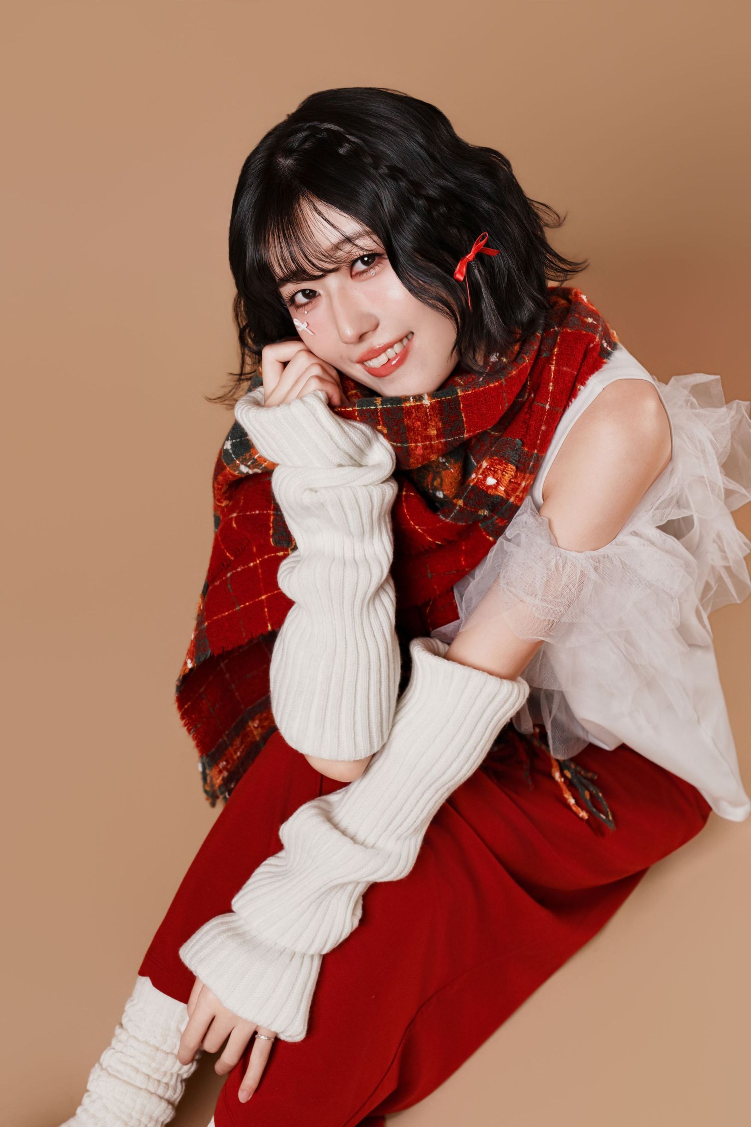 A person in a red dress and white knit sleeves poses playfully in a series of fashion portraits against a brown backdrop.