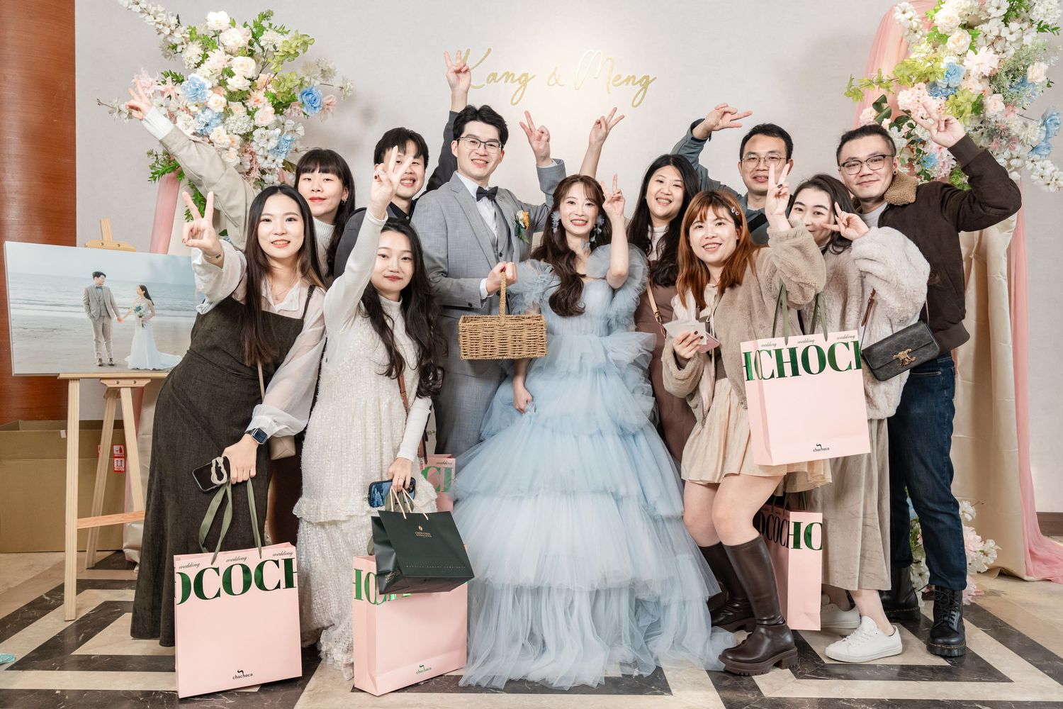 Wedding celebration with guests posing together at a reception decorated with pink and white floral arrangements.