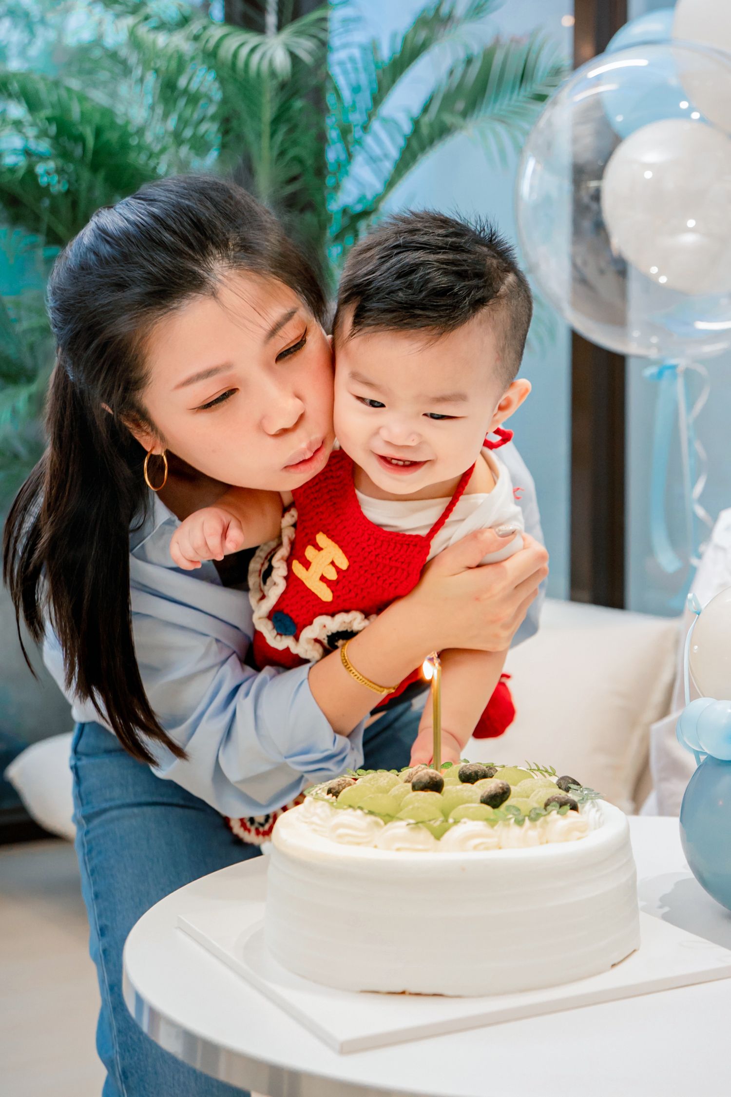 A joyful moment around a birthday cake with blue balloon decorations in the background.