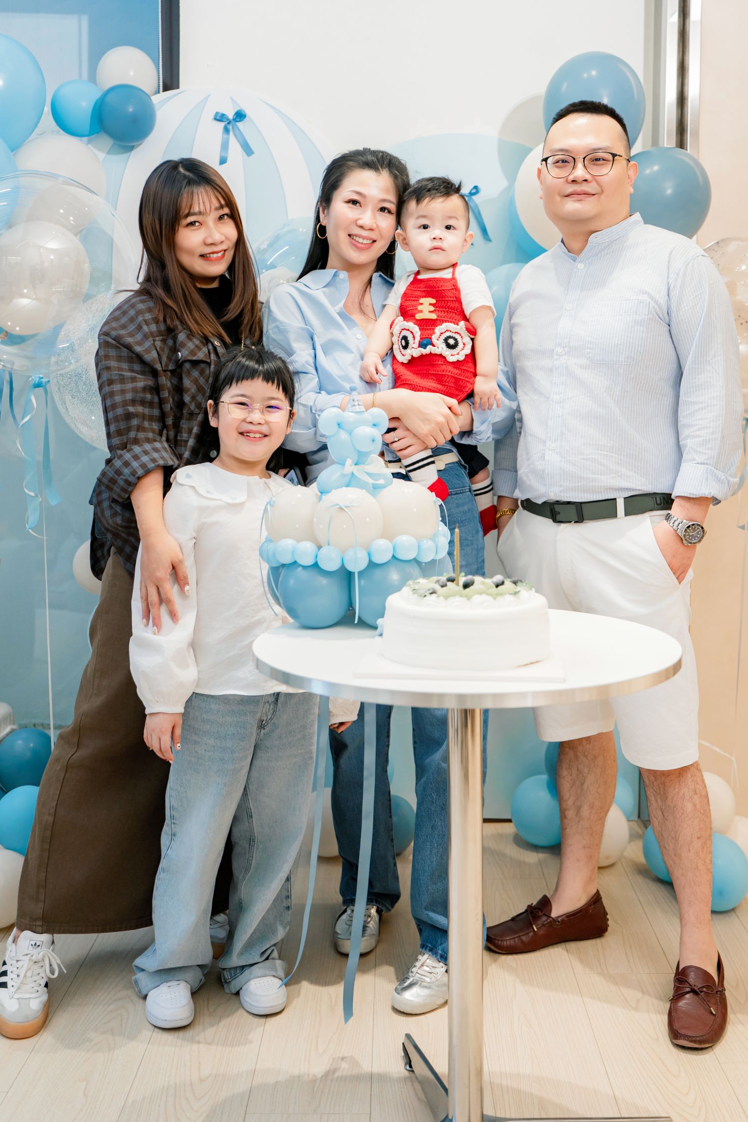 A collage of family photos at a baby's birthday celebration with blue balloon decorations and white cakes.