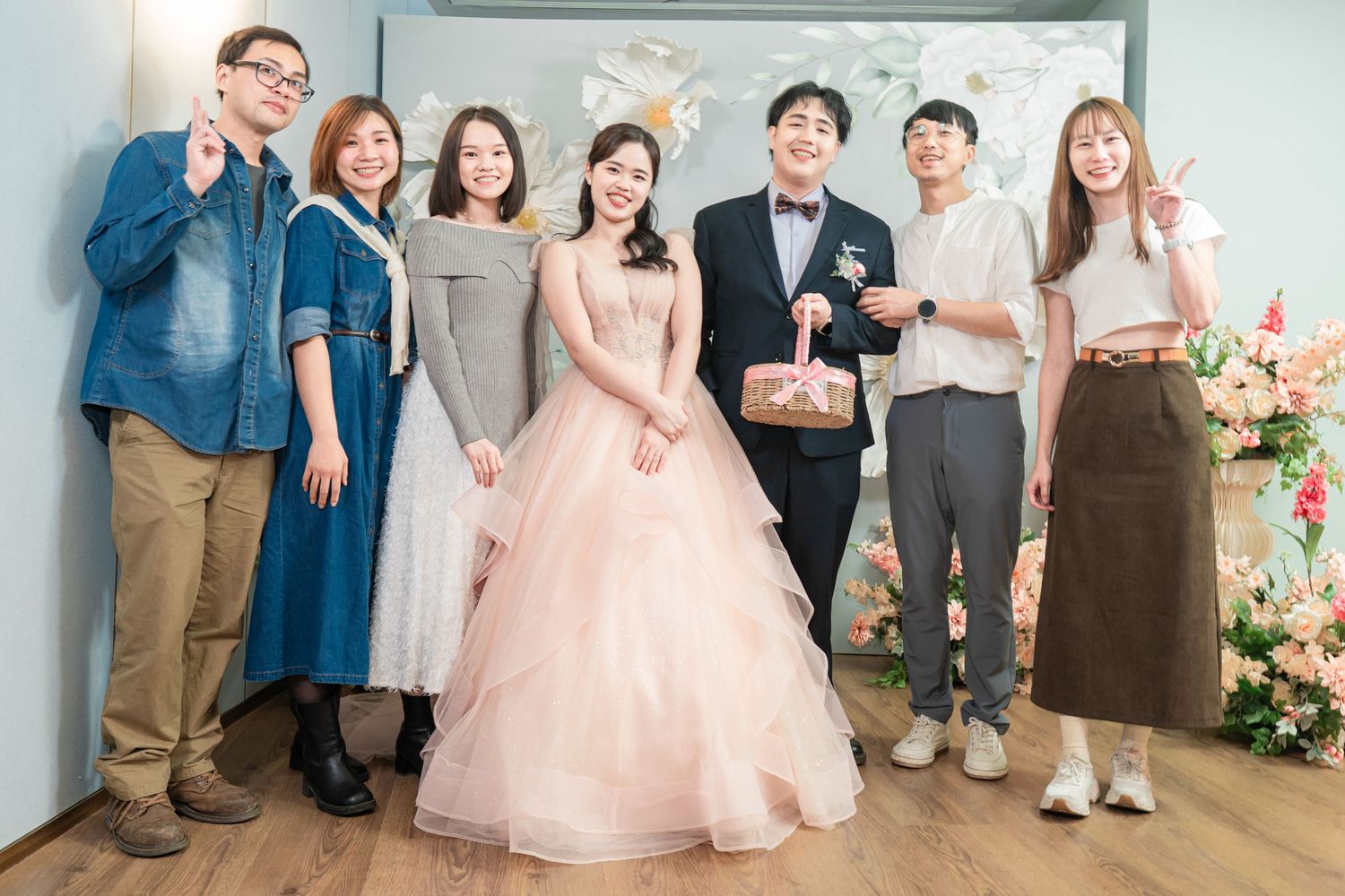 A group of people stand together in a hallway wearing formal attire including pink dresses and suits.