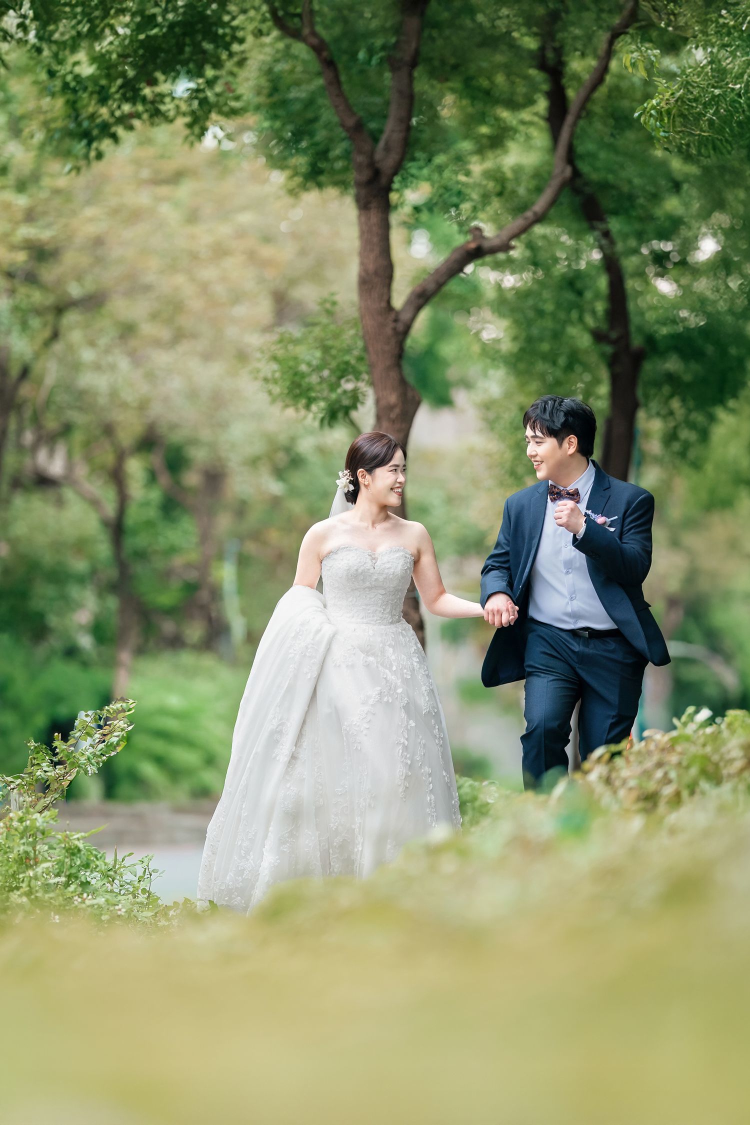 A couple in wedding attire shares romantic moments in a lush green garden setting during their photoshoot.