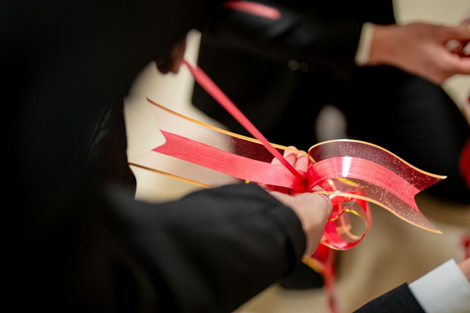 A hand holds a rolled up diploma tied with a red ribbon during a graduation ceremony.