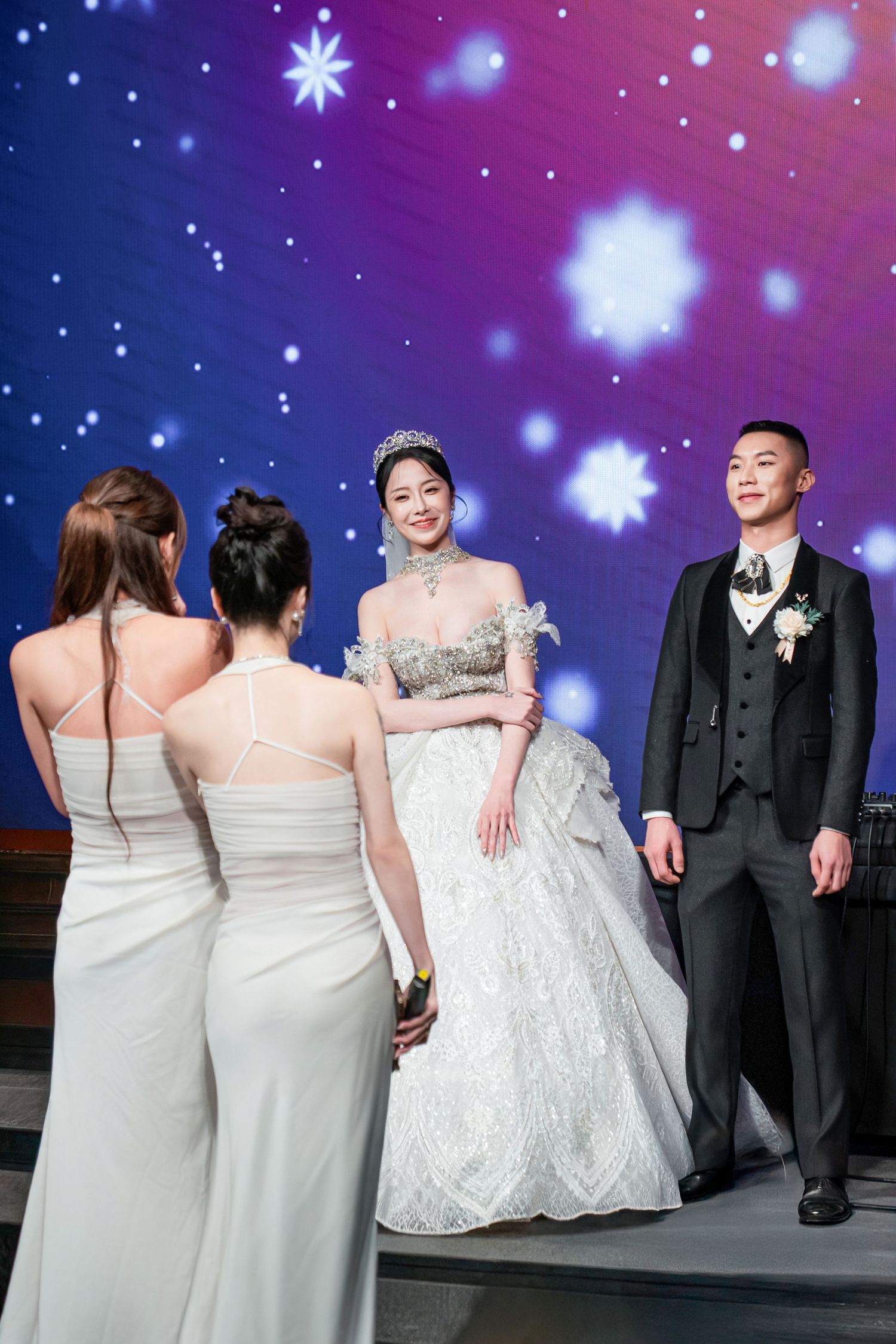 Wedding party members pose together under purple starry lighting effects at an evening reception celebration.