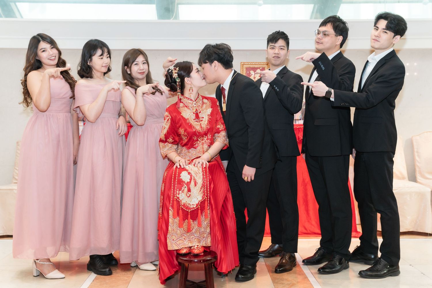 Wedding party members pose together with bridesmaids in pink dresses and a bride in traditional red qipao dress.