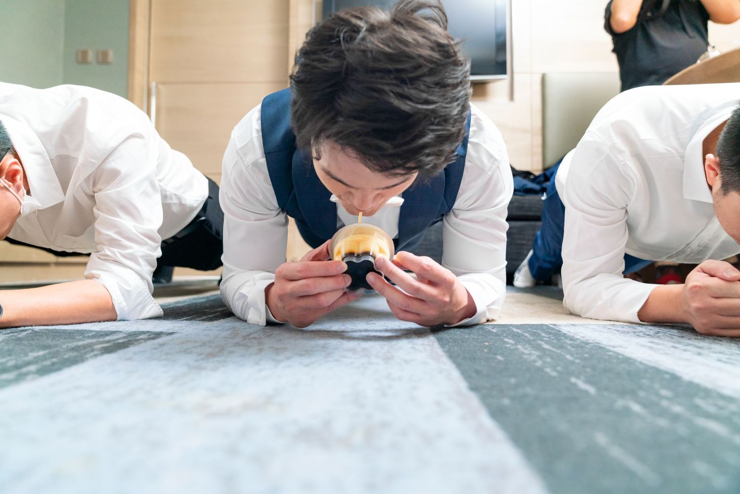 Three people in white uniforms lie on floor inspecting items up close in a professional setting.