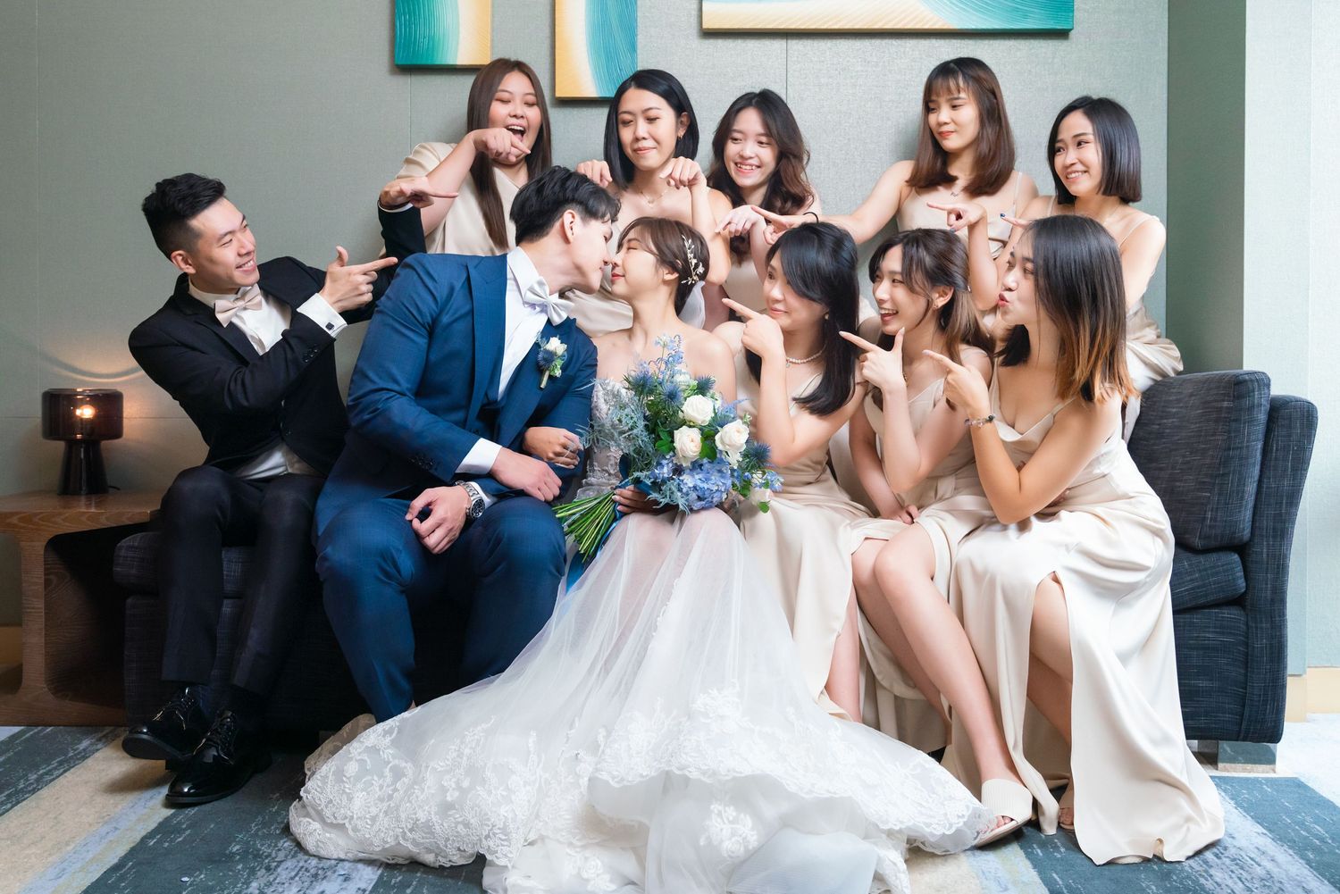 Wedding party sitting together on modern grey couch as they pose with champagne glasses during celebration.