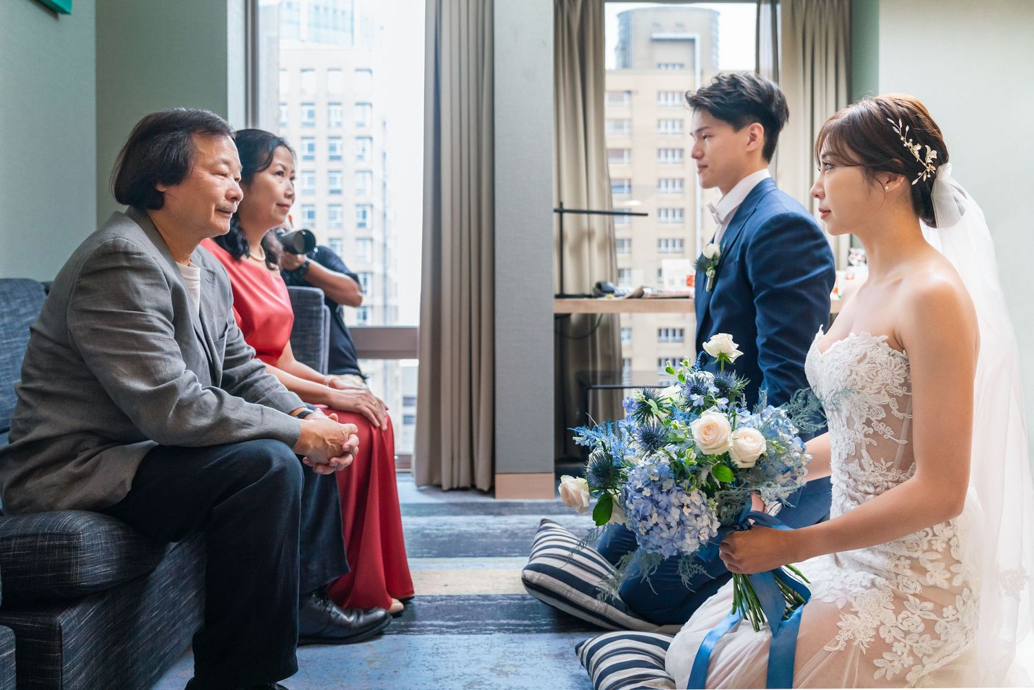 Joyful wedding moment captured at an indoor venue with guests, formal attire, and a bouquet of blue and white flowers.