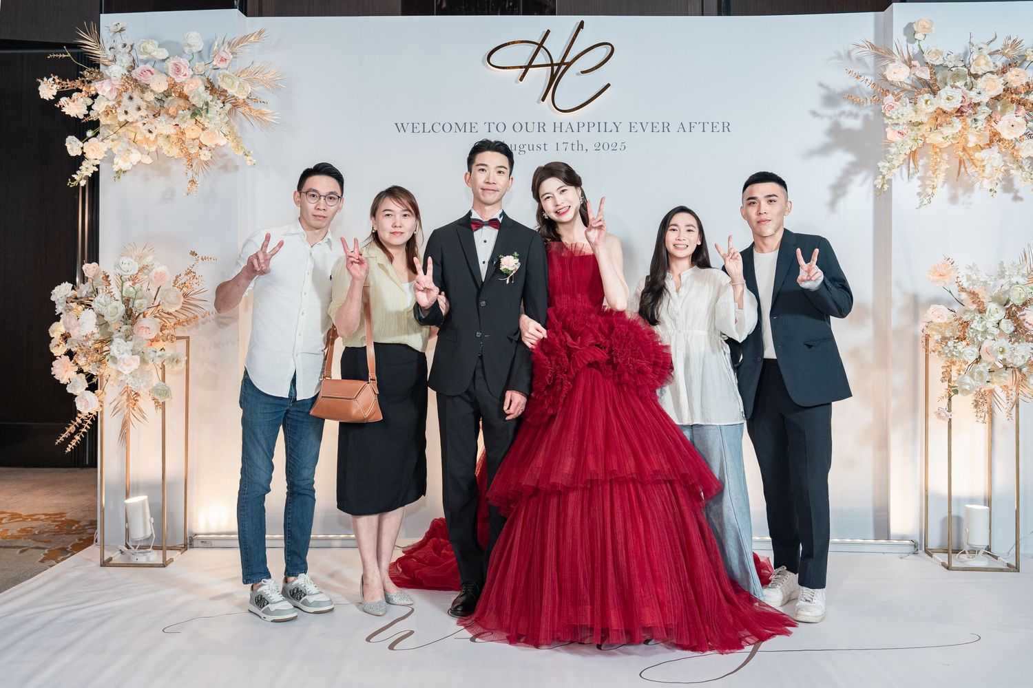 People pose for formal portraits in an elegant white room decorated with soft peach floral arrangements.