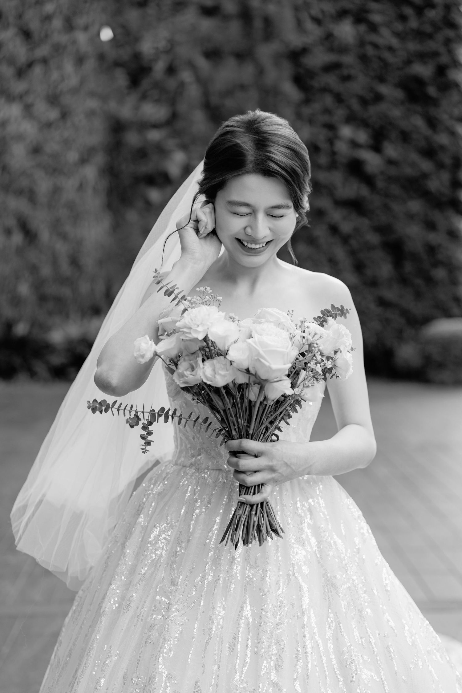 A joyful bride in a white lace wedding dress holds a beautiful bouquet of flowers while wearing a flowing veil.