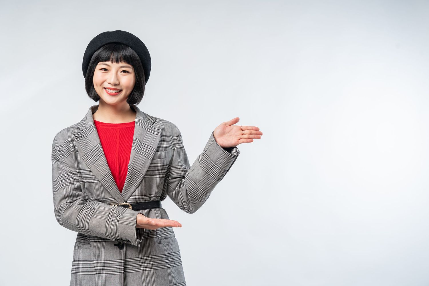 Professional in gray blazer and red top gestures welcomingly against white background.