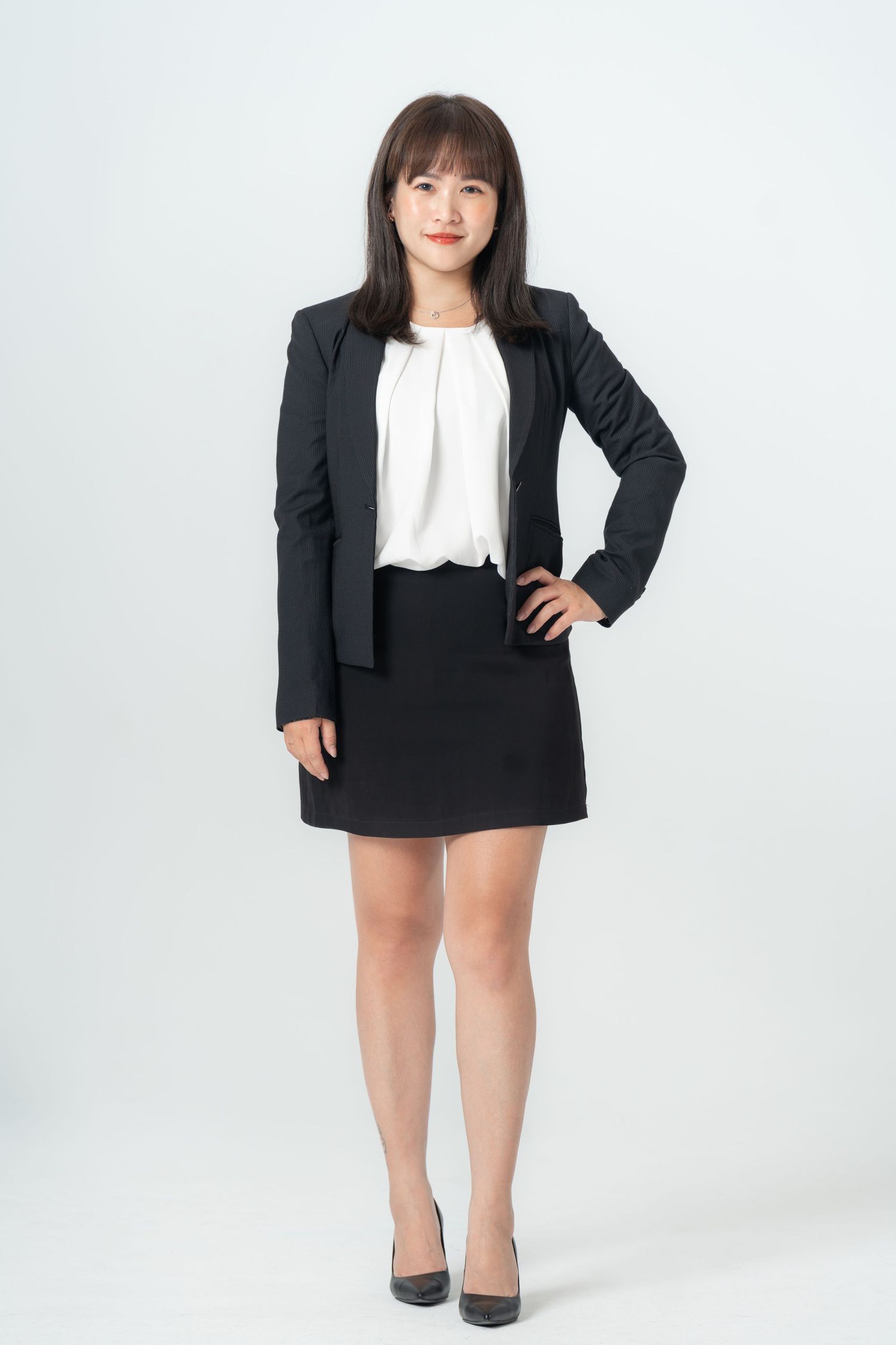Professional woman in black blazer and white blouse poses confidently against white background in studio setting.