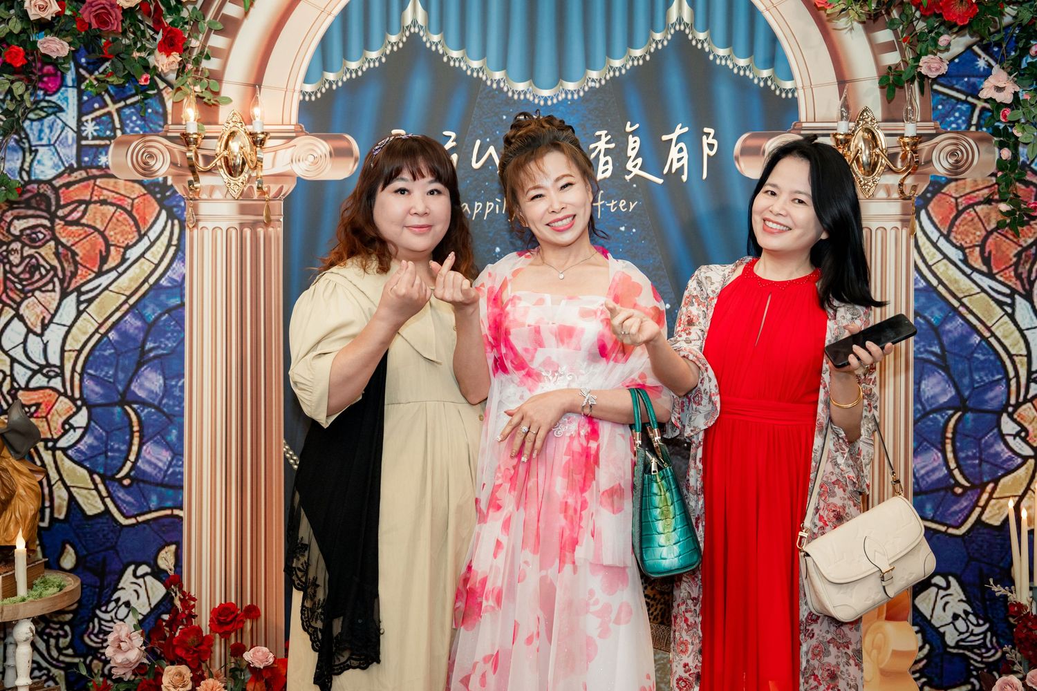Three women pose and smile together in front of an elegant decorative backdrop at a formal event.