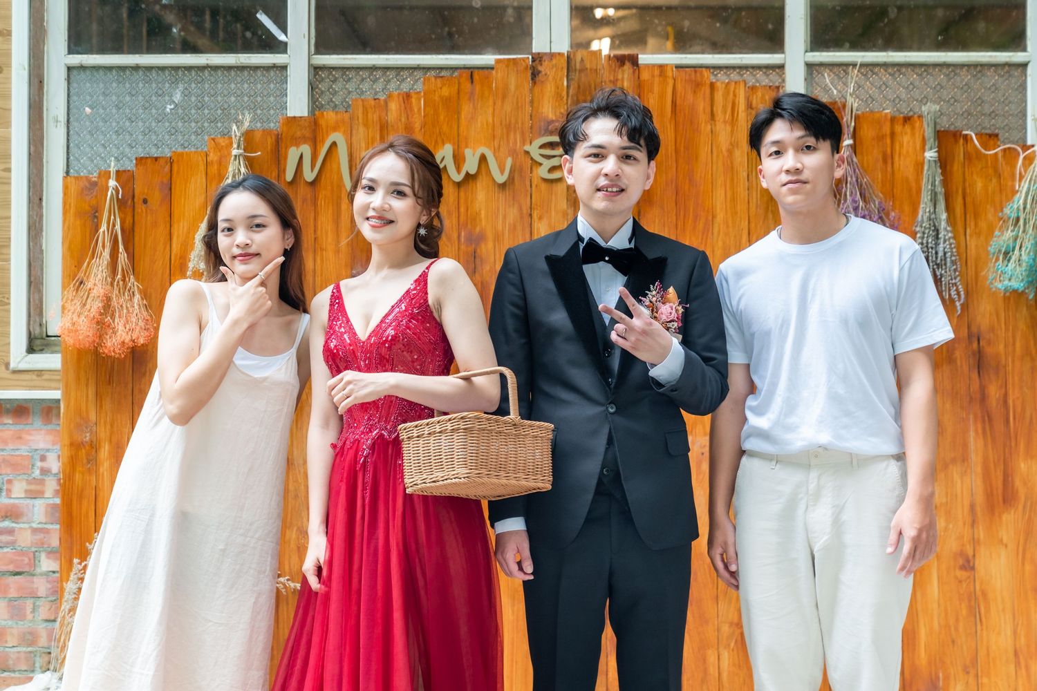 Four people in formal wear pose together against wooden backdrop with rustic decor elements.