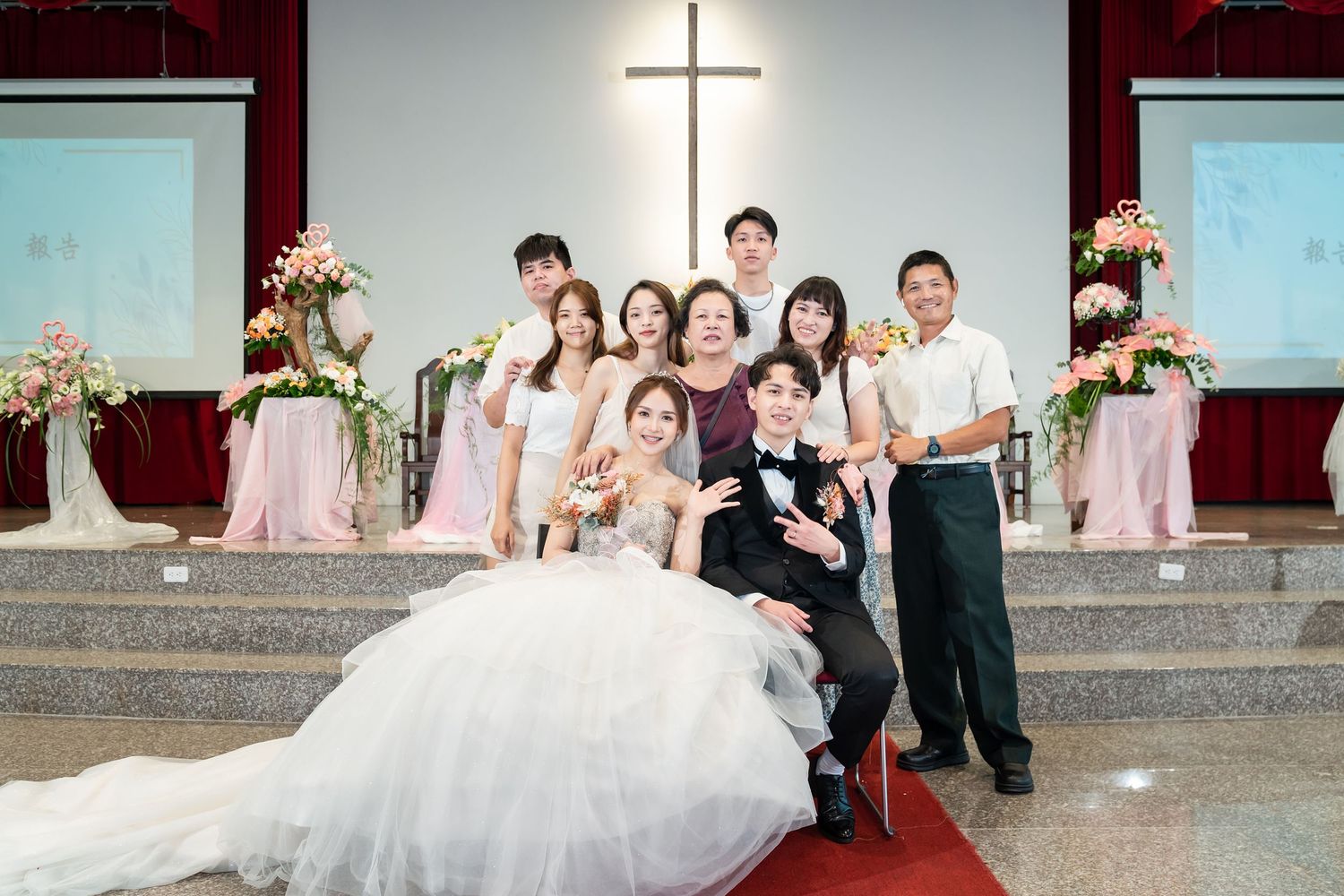 Wedding celebration in church with white cross and floral arrangements framing the group.
