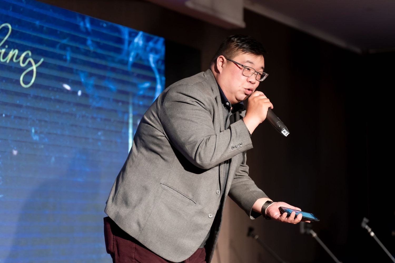 Speaker presents on stage with dramatic blue lighting and background effects.