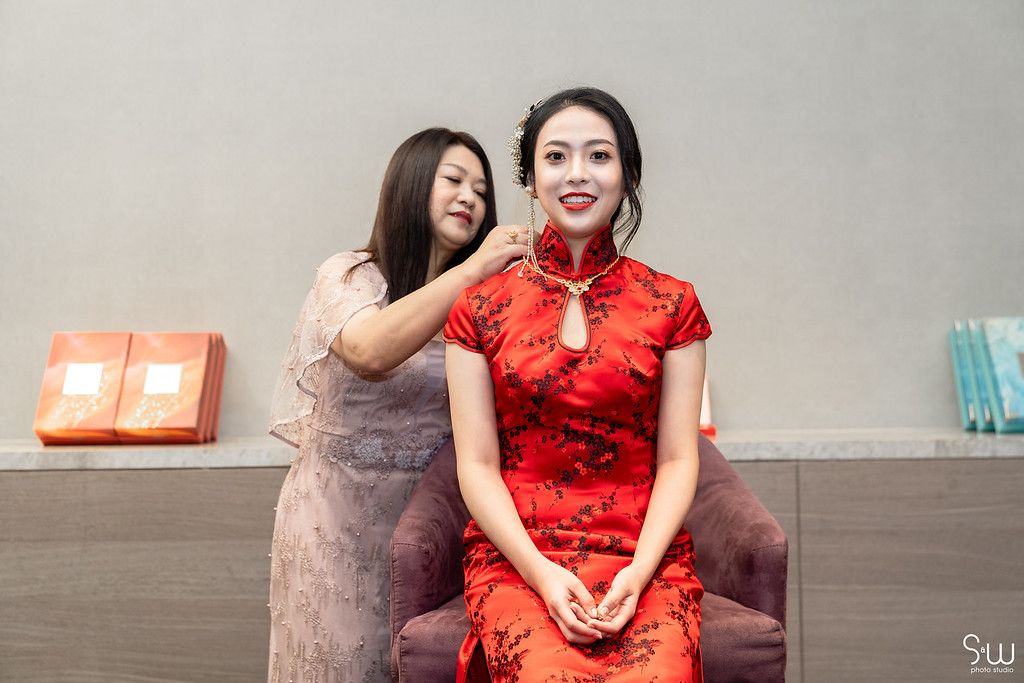 Two people sharing a moment during wedding preparations with one wearing a traditional red qipao.