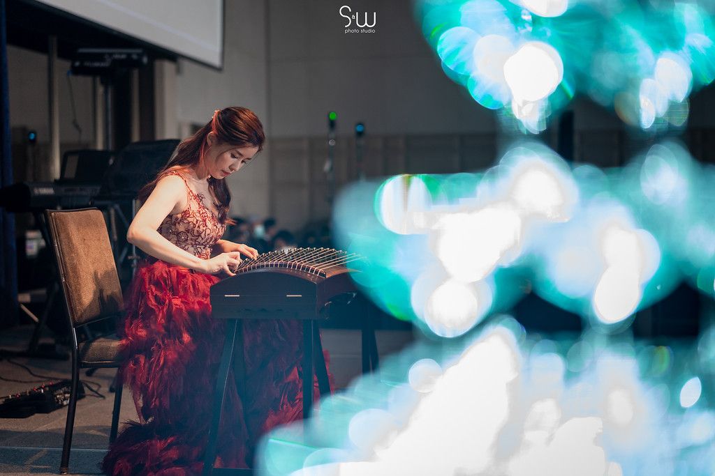 Woman in red dress performs at piano with bokeh lights in background.