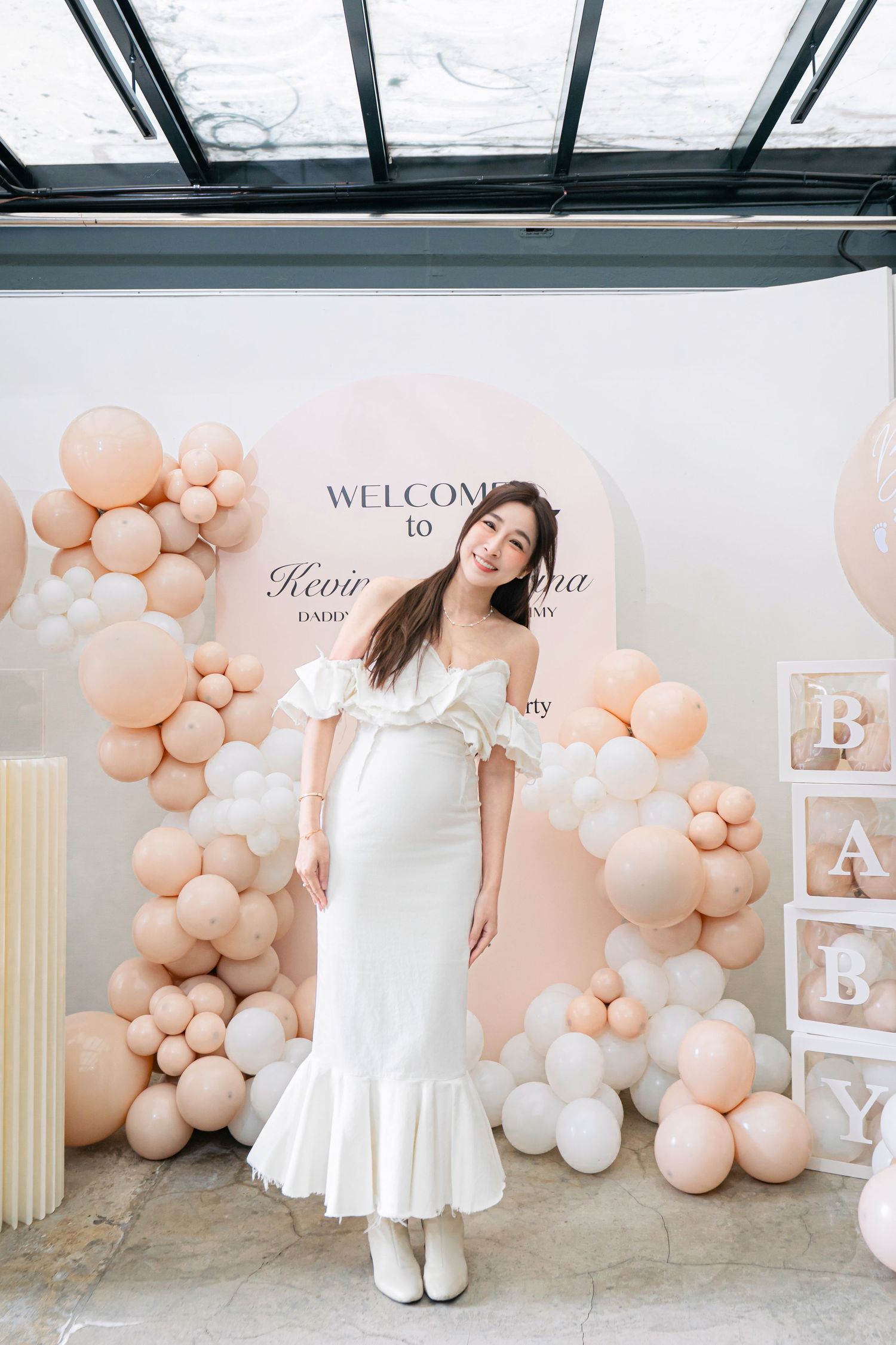 Elegant baby shower setup with blush pink balloon garland and white decor against a neutral backdrop.