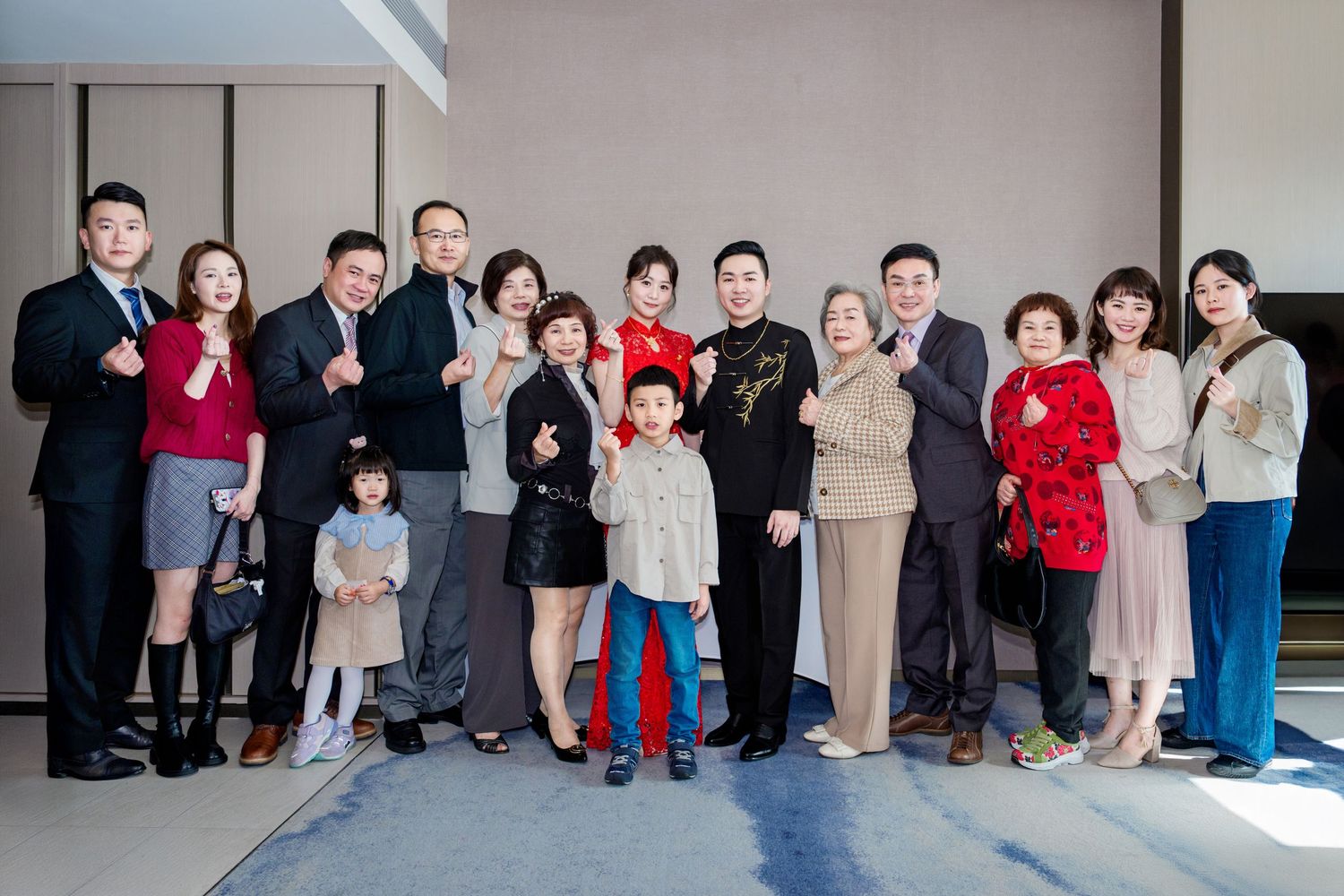 A large family group in coordinated winter outfits poses together against a gray wall in an indoor setting.
