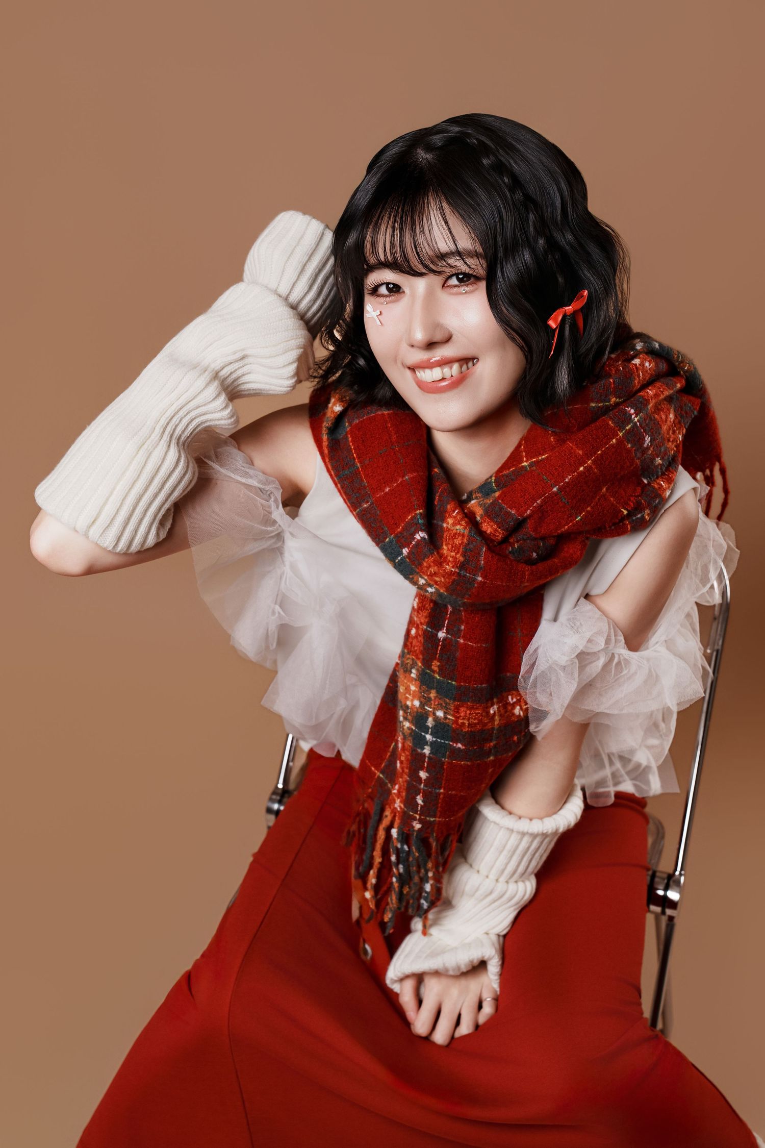 A person in a white sweater and red plaid scarf poses playfully in a series of studio portraits against a brown backdrop.