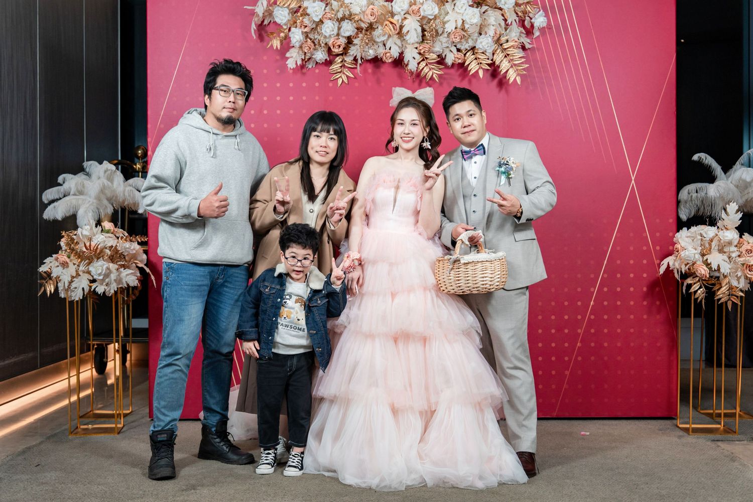 A group stands together against a pink backdrop with floral decorations at a formal celebration event.