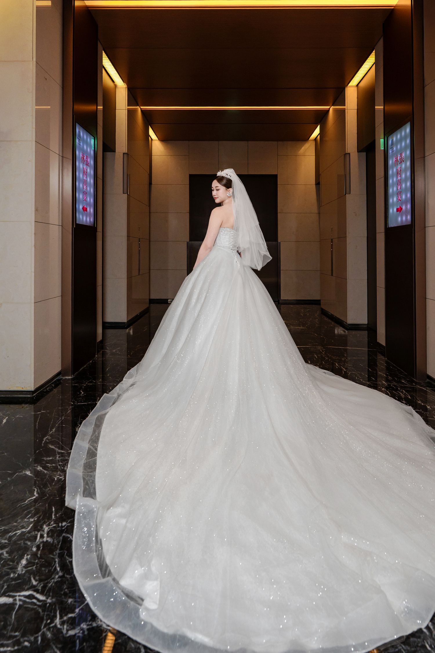 A bride in a stunning white cathedral-length wedding gown with a dramatic long train stands in an elegant hallway.