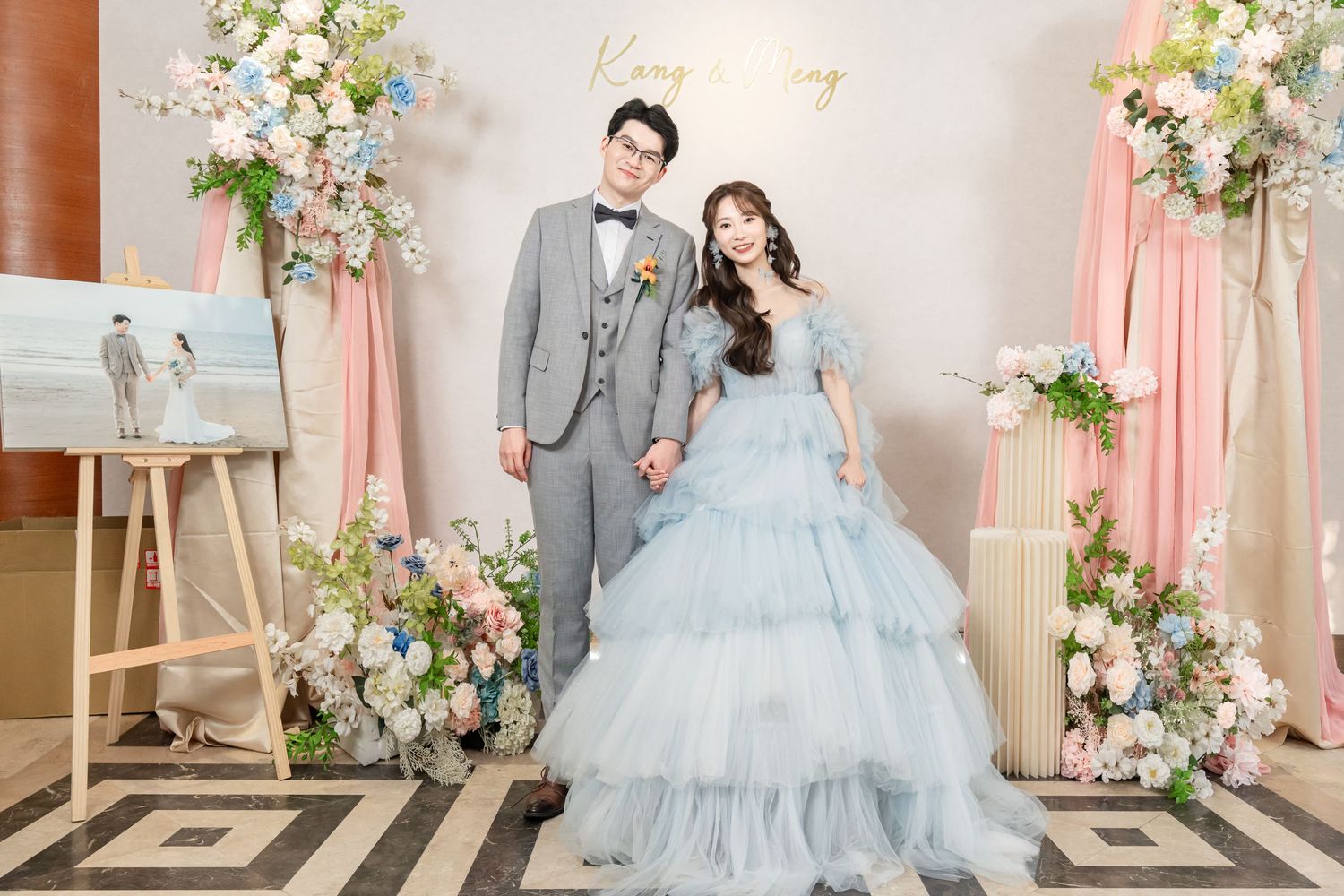 A romantic wedding photoshoot featuring soft blue and pink decor with floral arrangements and elegant attire.