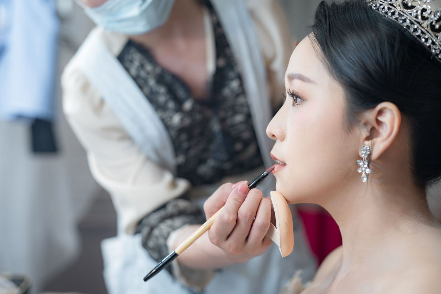 Professional makeup artist applies lipstick to bride during wedding day preparations.